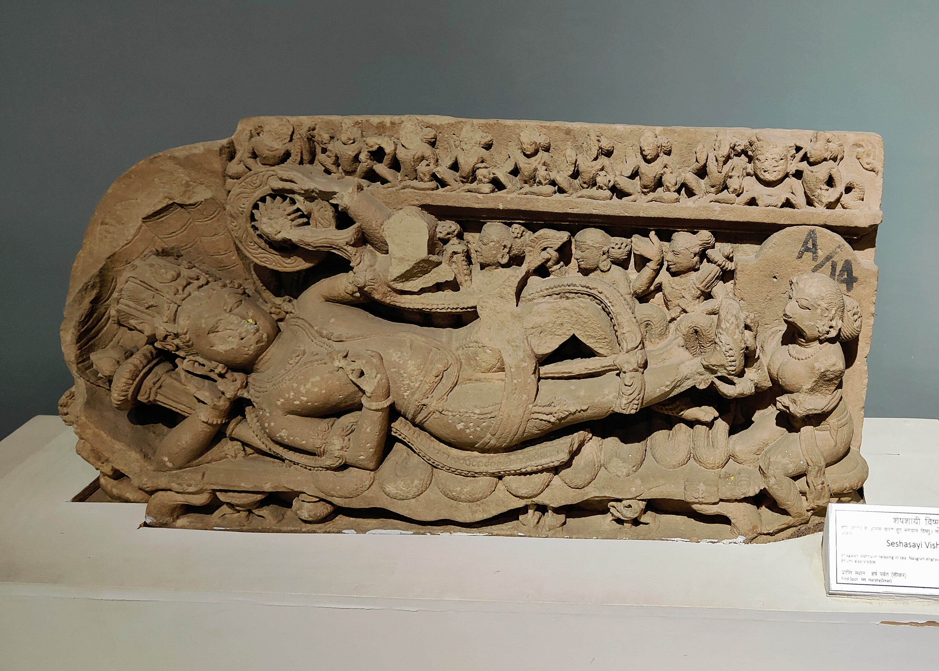 The image in question depicts Shesashayi Vishnu, or Vishnu, in a reclining position on the serpent. It was retrieved from Harsha Hill and is now housed in the Government Museum, Sikar. Lord Shesa likely served as the main cultic image inside a now-lost Vaishnava shrine. The image features representations of the nine planets, with Lakshmi tending to Vishnu at his feet. Behind him are three ayudhapurusa, personifications of his weapons.