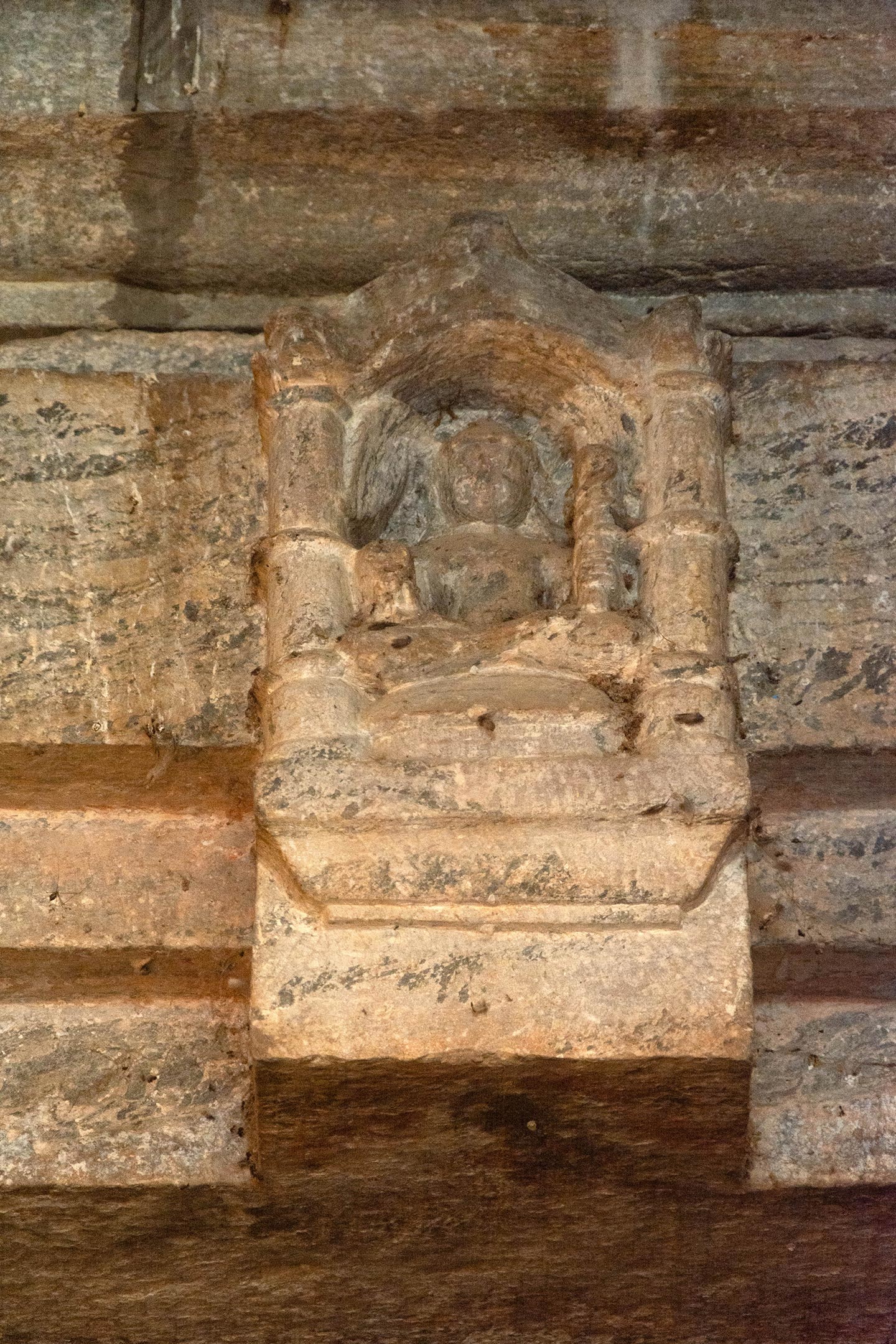 Image 1: The lintel of the sanctum-doorway shows a two-armed depiction of Lakulisha seated in padmasana in dhyanmudra, carrying a lakuta, or club, in his left hand and fruit in his right hand—part of his standard iconography—inside a niche on the lalatabimba.