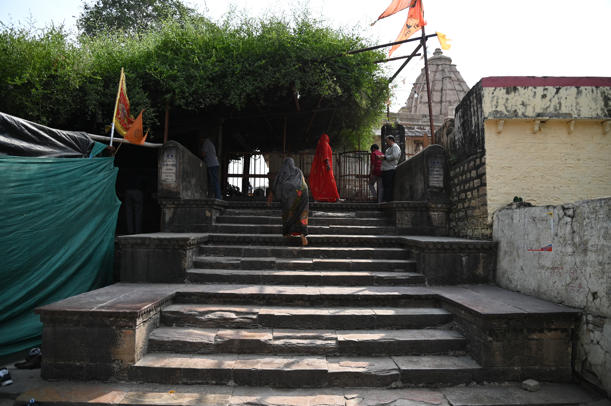 There are stairs that lead to the temple, which is situated on an elevated area. To provide a sitting place for the devotees, stone platforms or benches are placed on both sides of the steps.