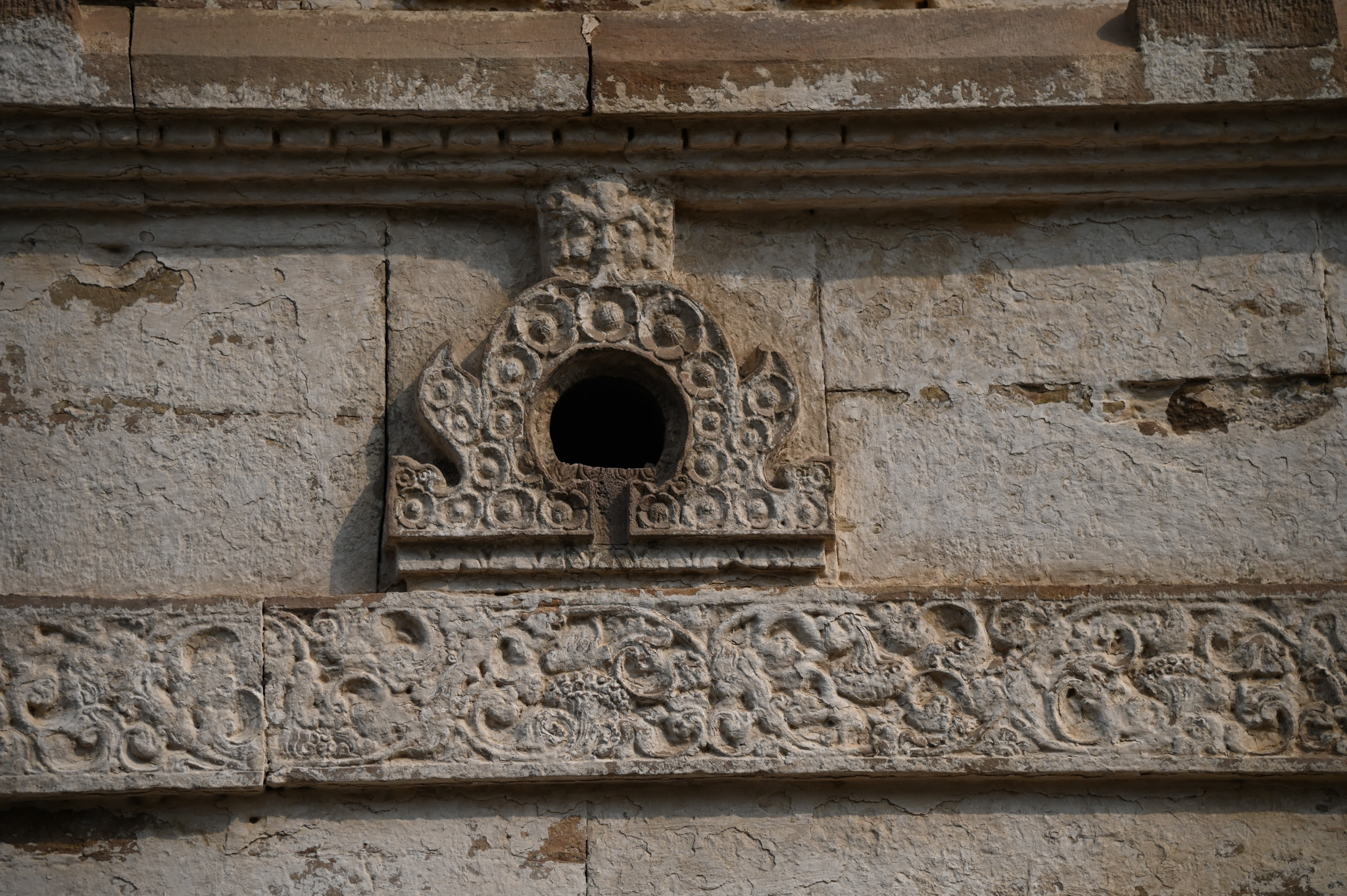 The jangha (wall) of the garbhagriha (sanctum sanctorum) has a broad floral scroll that runs across all three walls and divides the wall into upper and lower parts. Two beautiful Chaitya arch motifs adorn this band on the rear wall. A grassamukha at the arch's apex emits the flowers that decorate the chaitya arch.