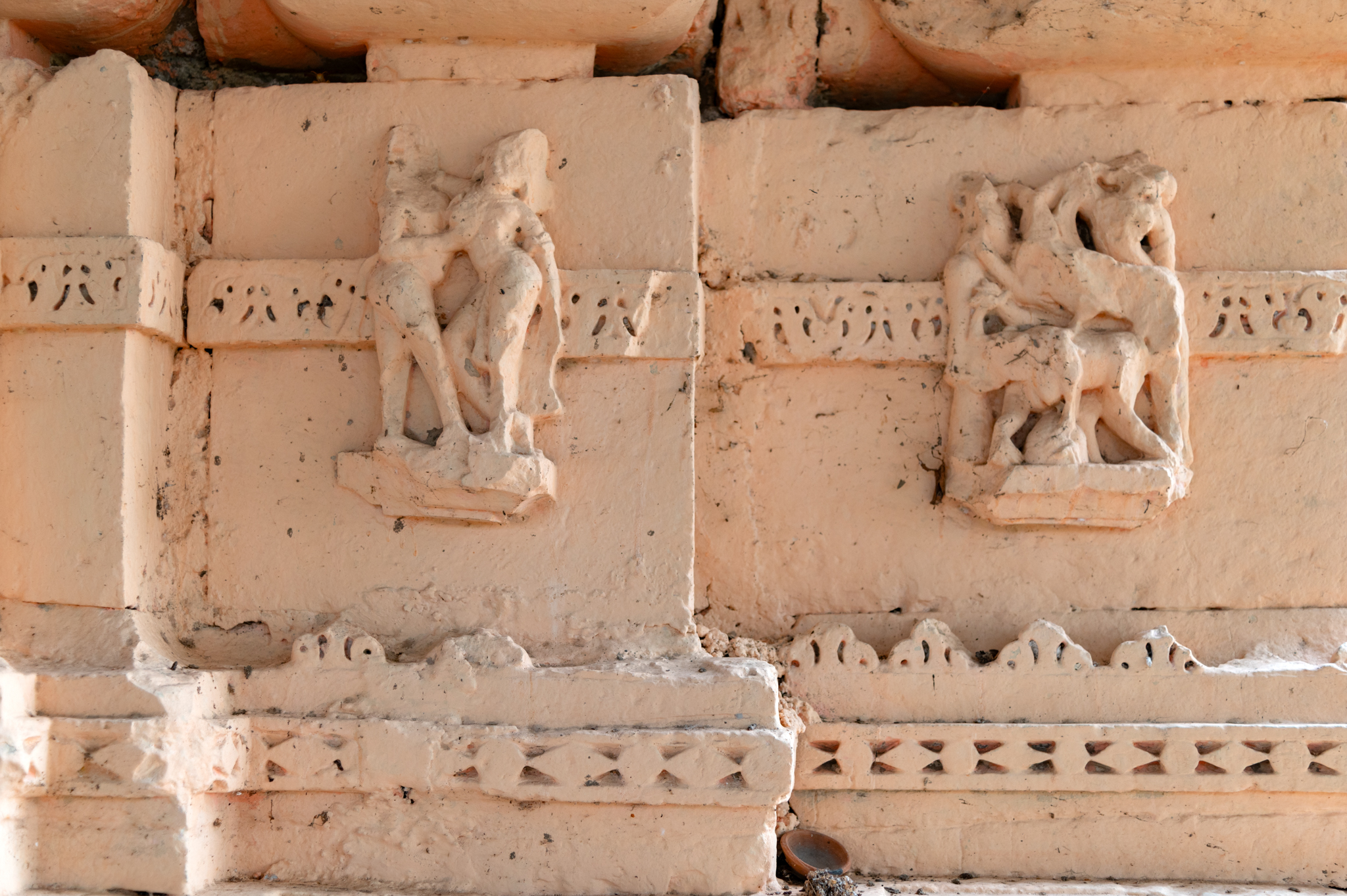 The kumbha, a moulding on the vedibandha of the garbhagriha, features figures of deities, apsaras, mithunas, and maithunas. Both the mithuna and maithuna imagery are visible here. Mithuna represents a couple embracing each other, where the male figure is softly pressing his partner’s breast. The maithuna, next to the couple, depicts four figures engaged in amorous activities.