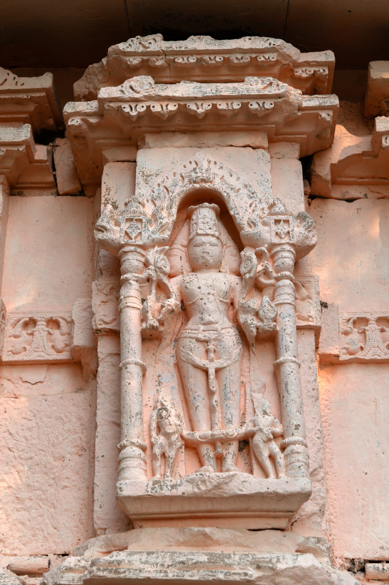 The garbhagriha's rear wall features a projection depicting a syncretic image. This image depicts Surya, Vishnu, and Shiva coming together to form a deity called Hari-Hara Hiranyagarbha. The image depicts the deity with three heads and six arms, standing alongside his attendants Dandaka and Pingala. Adorned with a beautiful crown and jewellery, the deity is wearing knee-length boots, which confirms that the frontal face and body represent Surya, who is shown holding flowers in both his hands. In his upper hands, one can notice sarpa (snakes), an attribute of Shiva, while his lower arms hold a shankha (conch shell) and chakra (discus), symbols associated with Vishnu.