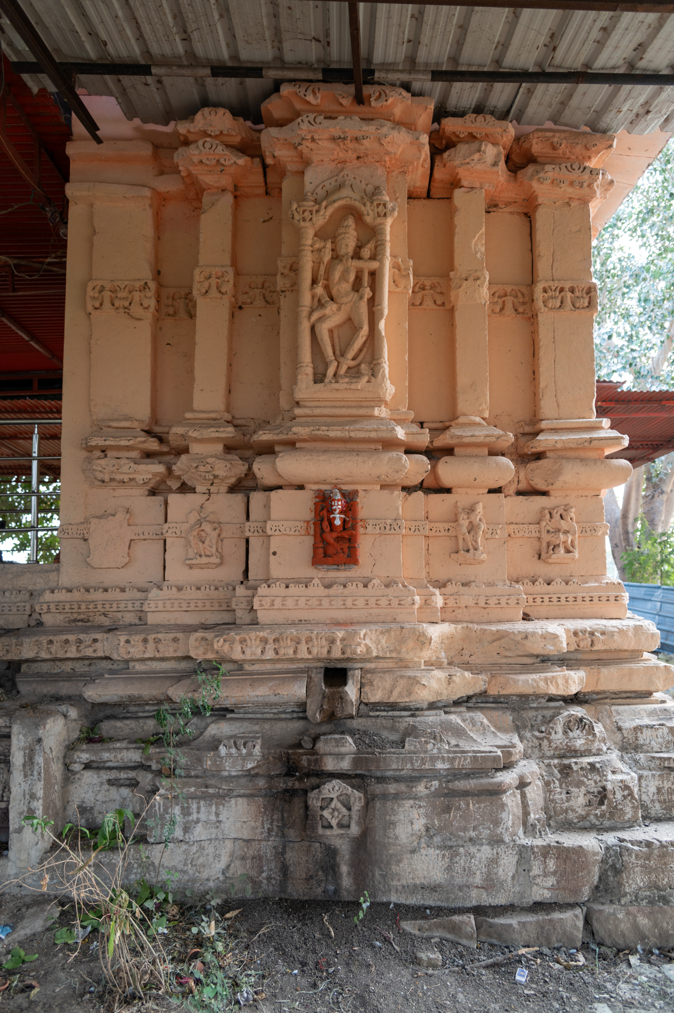 The jangha on the south wall of the garbhagriha depicts Chamunda in the bhadra. The depiction shows the six-armed goddess standing on a human body. She is holding a knife, trishula (trident), and damaru (hourglass-shaped drum) in her right hand. In her left hand, she is holding a bowl and a khatwang (staff with a skull at the top), and in her middle hand, she is touching her lip. Her body appears emaciated, her breasts dry and saggy, and her belly sunken. She sports a jatamukuta and adorns herself with ornaments. It is worth noticing that she is wearing a snake as her waist belt.