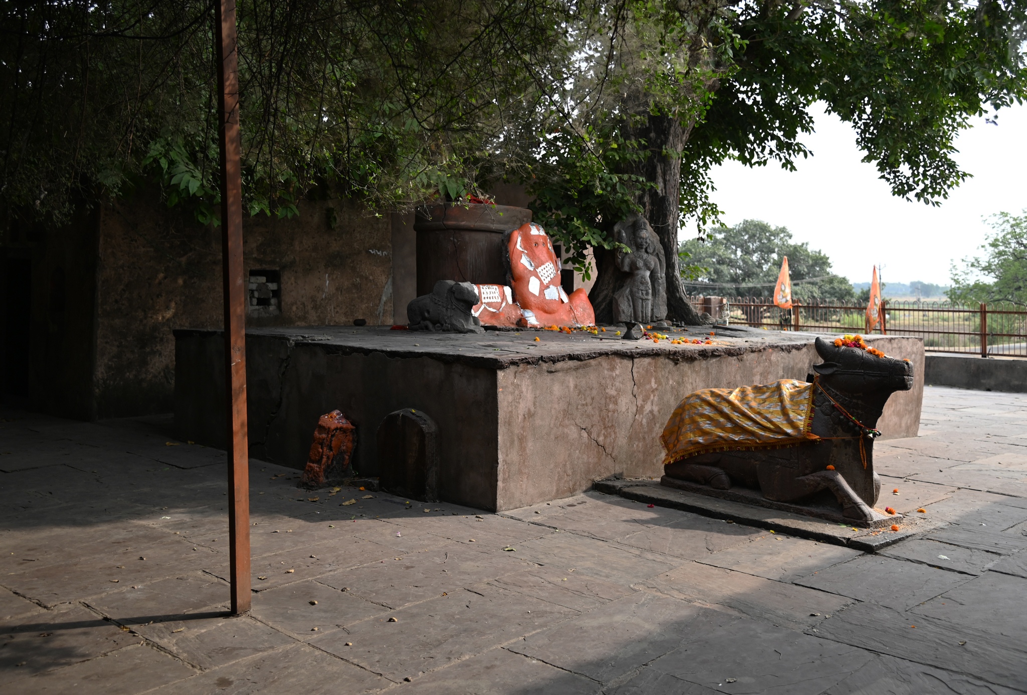 Image 2: In front of the entrance to the mulaprasada (main temple) inside the complex, there is a platform with ancient stone sculptures of a goddess (probably Parvati), Ganesha (covered in vermilion), and a small Nandi. A larger Nandi figure stands directly in front of the temple.