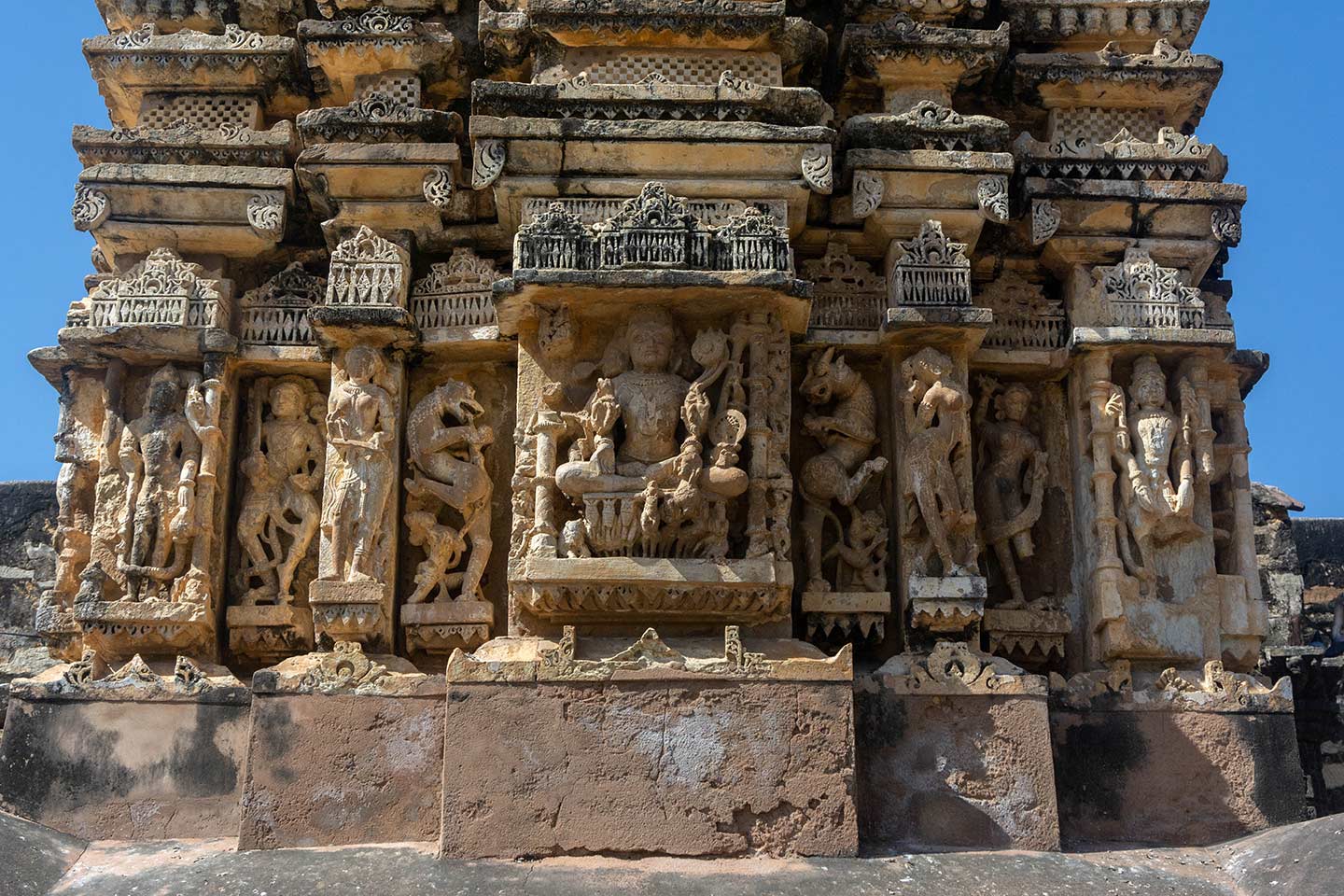 This is the east-facing elevation of the central shrine in the Neelkanth Mahadev Temple. The bhadra (central projection) image on the exterior wall facing east contains a unique composite image called the Harihararka (or Hariharapitamaharka), which is a depiction of Shiva, Vishnu, and Surya (and plausibly Brahma) incorporated into one sculpture. Sitting on a chariot of seven horses, the three-faced figure embodies the attributes of all its representative deities.