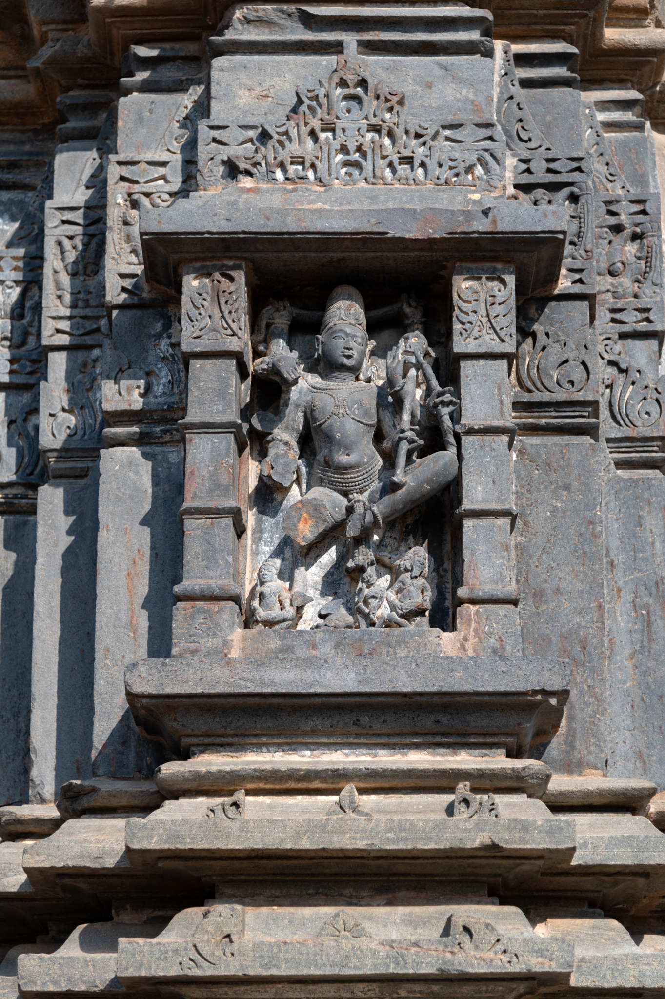 The Mandaleshwar Mahadev Temple's west-facing central projection features an icon of Natesha. A decorative niche with a pediment above frames the image. The six-handed sculpture has a broken right side. The sculpture shows the lower left and upper left hands holding a khatvanga (staff with a skull).