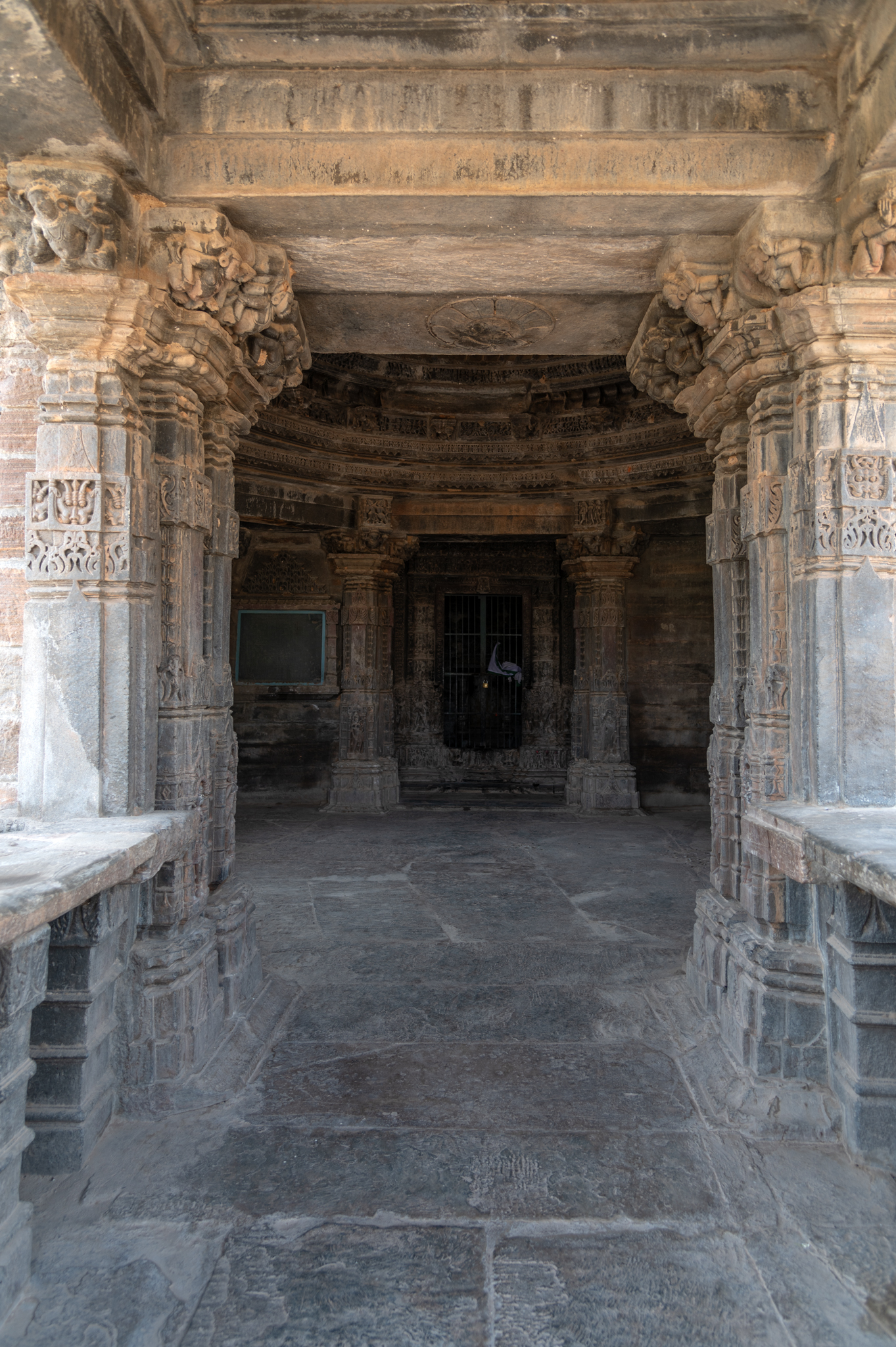 The Mandaleshwar Mahadev Temple's mandapa, or hall, is visible from the temple's mukhamandapa, or front porch. Ashtylar mandapa halls have no central pillars. The pilasters are arranged along the sides to support the entire structure. The pilasters and pillar types are simple, plain shafts with minimal ornamentation of foliage motifs.