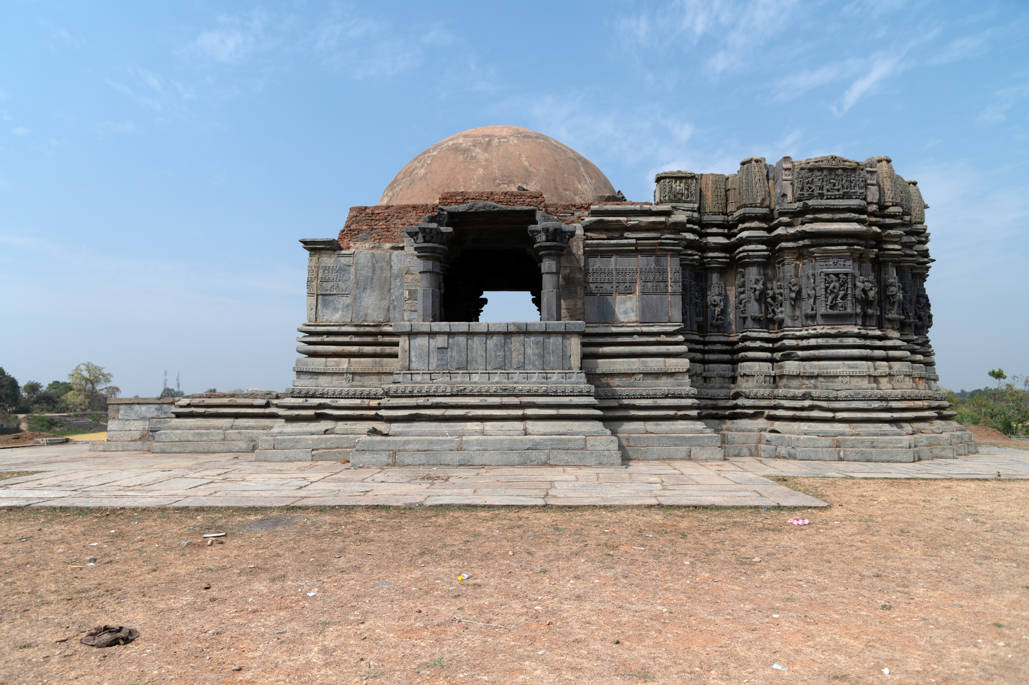 This is the south-facing elevation of the main central shrine of the Kumbheshwar Mahadev Temple complex. According to its plan, the temple consists of a mukhamandapa (front porch), a mandapa (pillared hall), antarala (vestibule and antechamber), and a garbhagriha (sanctum sanctorum). The mukhamandapa facing east-west has not survived, barring its plinth. A row of kutas (aedicules) is visible above the main shrine, which indicates that the temple must have been adorned with a shekahri shikhara (multi-spired superstructure). On the south elevation's bhadra (central projection), there was a sculpture of Tripurantaka Shiva.