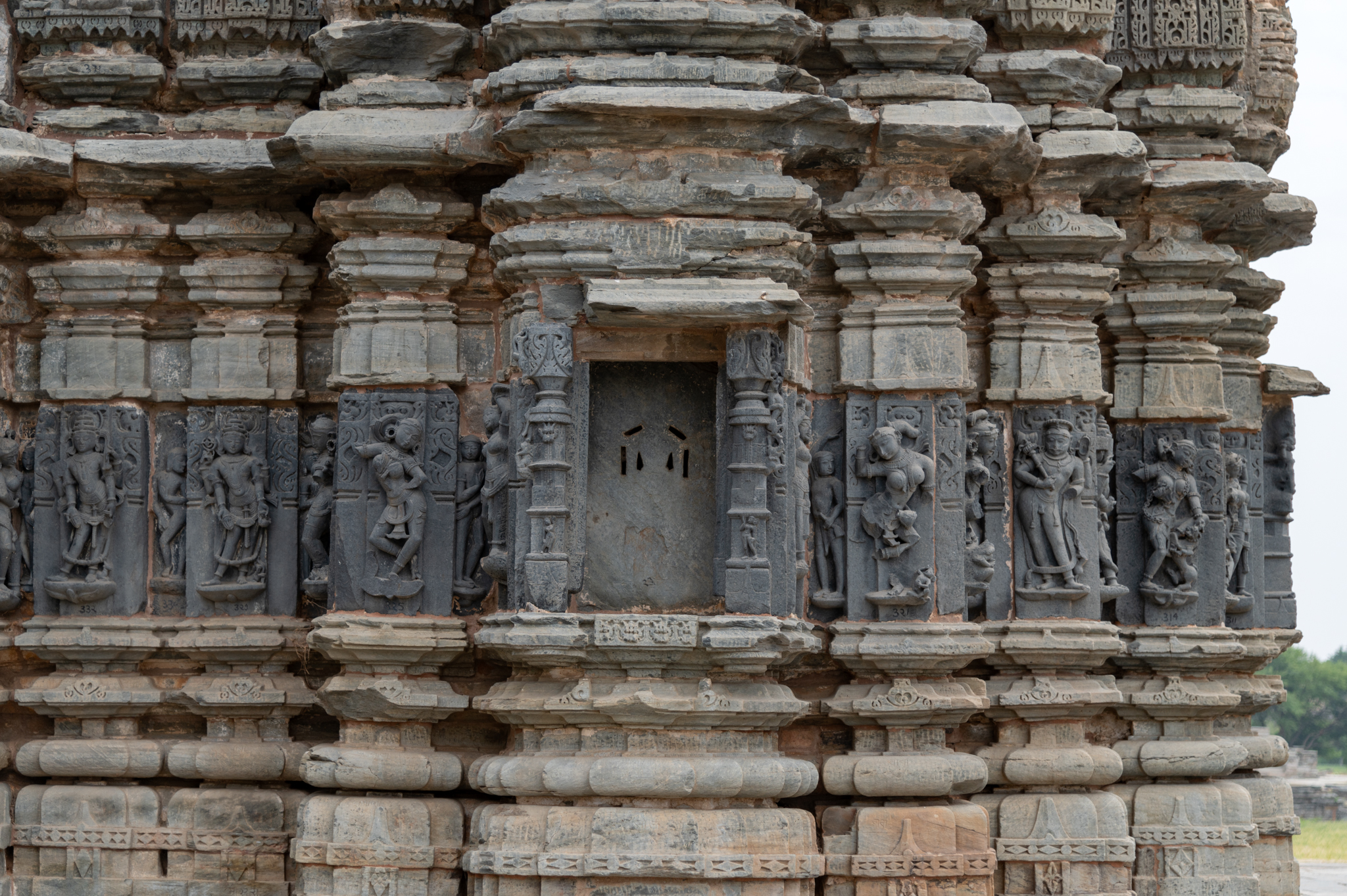 This is a view of the west-facing jangha (wall) of the Jain Temple, where the bhadra (central projection) niche is empty, but the intermediate and corner projections feature sculptures on both sides. The intermediate projections have depictions of dikpalas (deities of the cardinal directions). The recesses have depictions of ascetic figures.