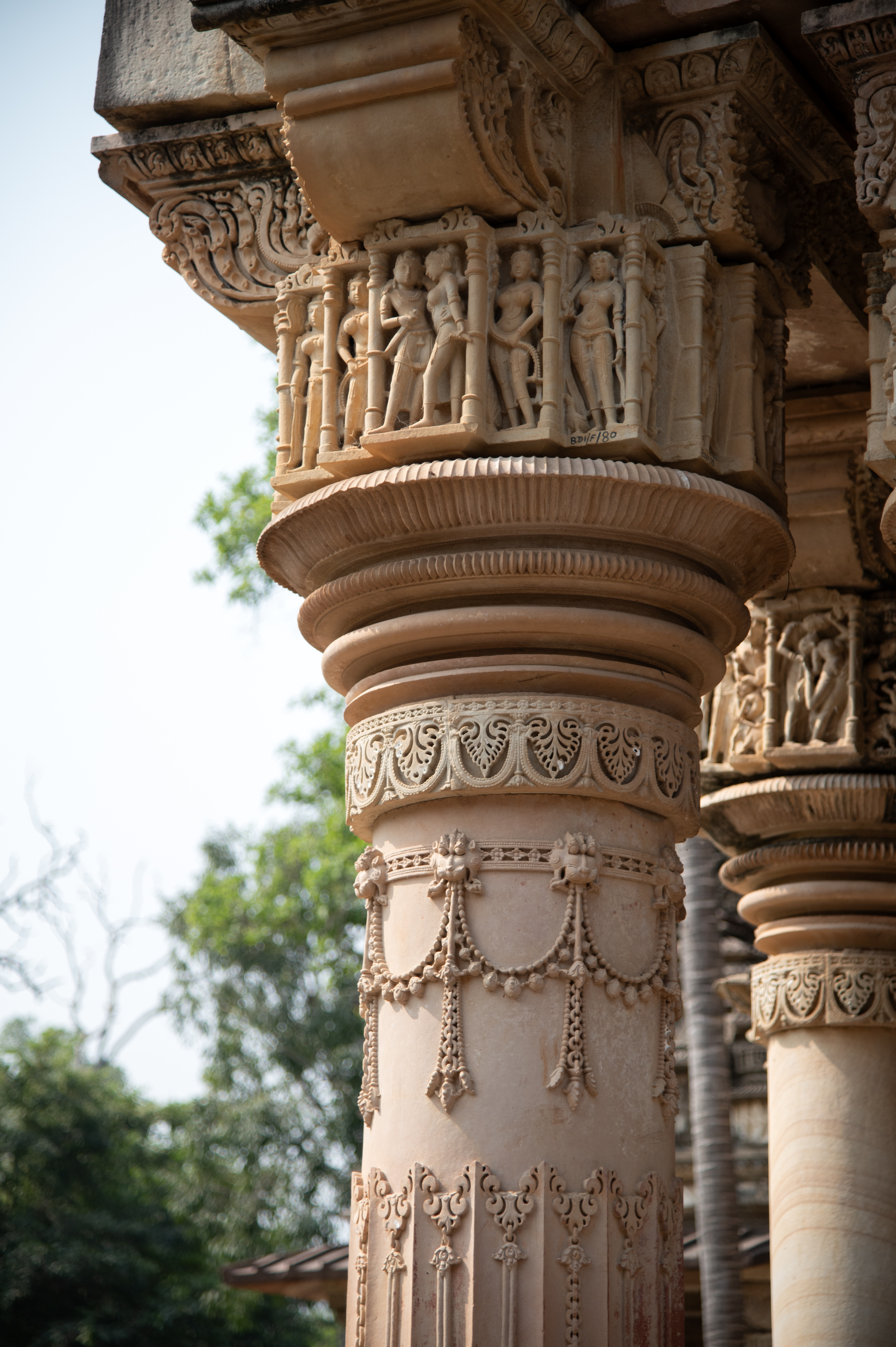 The top portion of the pillars of the mukhamandapa (front porch) shows couples engaged in different activities such as love-making, dancing and tender gestures, such as a male figure removing a thorn from his partner’s foot and kissing. On the proper right pillar of the mukhamandapa, one panel shows a couple carrying weapons and embracing each other. The couple is flanked by beautiful female figures holding garlands and scarves.