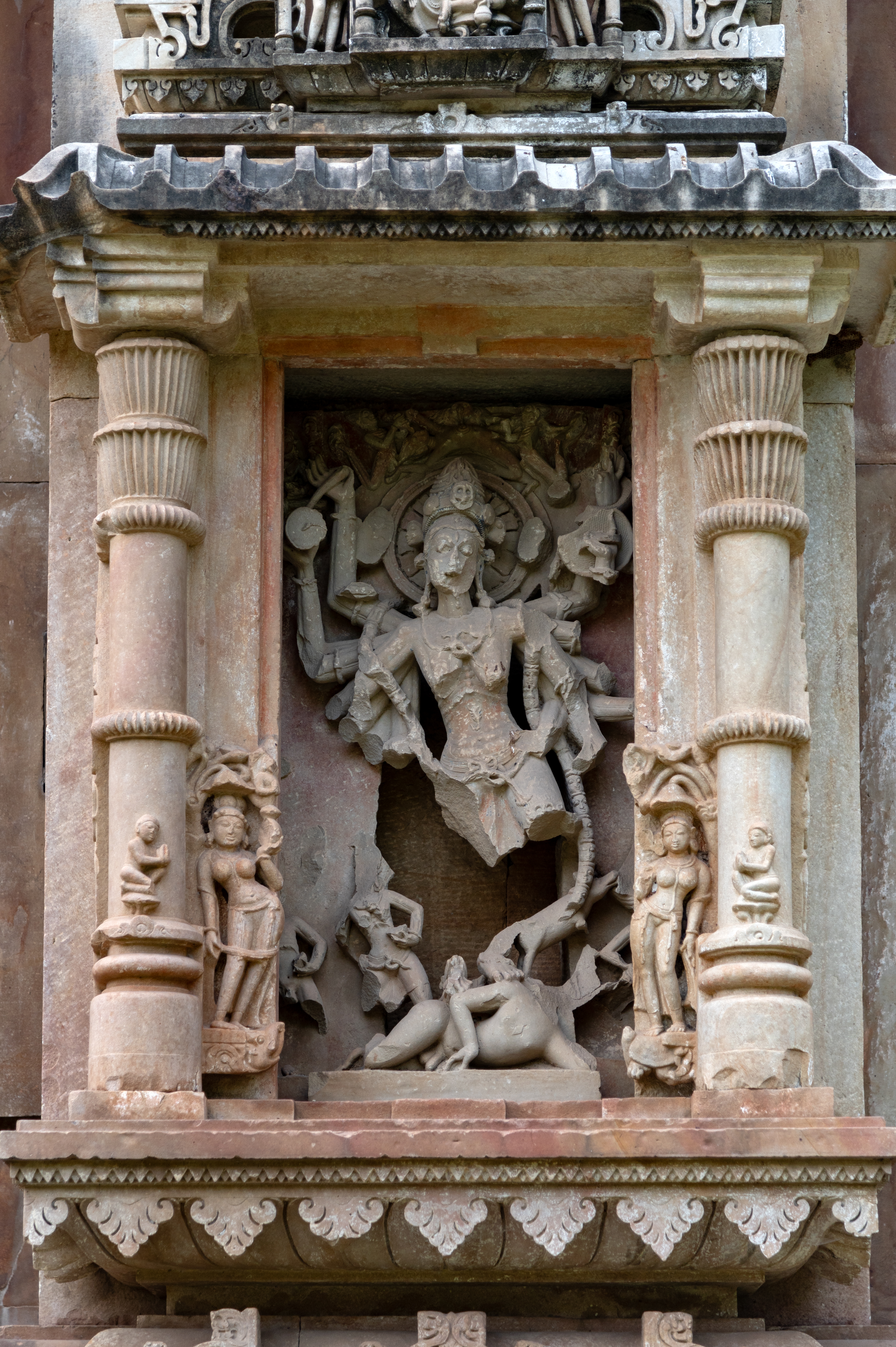 On the north wall of the garbhagriha (sanctum sanctorum), Chamunda is depicted with multiple arms, standing on a human body. All her arms are broken except her upper three arms, one of which is carrying a shield. She has a halo around her head with flying celestial shown on both sides of her halo. She has a jatamukuta (crown of matted hair) decorated with a human skull. Her face is damaged, but one can see bulging eyes. She has a thin body with shrivelled breasts and a sunken belly.