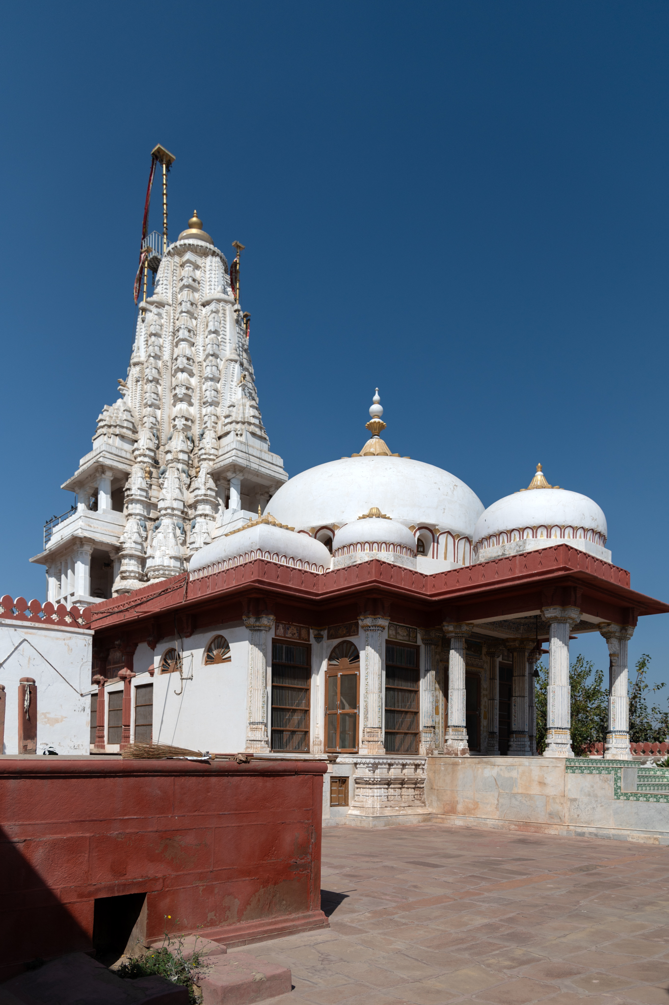 View of the Bhandasar Jain Temple as seen from the northeast corner of the complex. Built in the shekhari style of temple architecture, the temple has an imposing shekhari shikhara (multi-spired superstructure). The plan of the temple consists of a garbhagriha (sanctum sanctorum), mandapa (pillared hall) and a mukhamandapa (front porch). Domes roof the mandapa and shekhari shikhara is atop the garbhagriha.