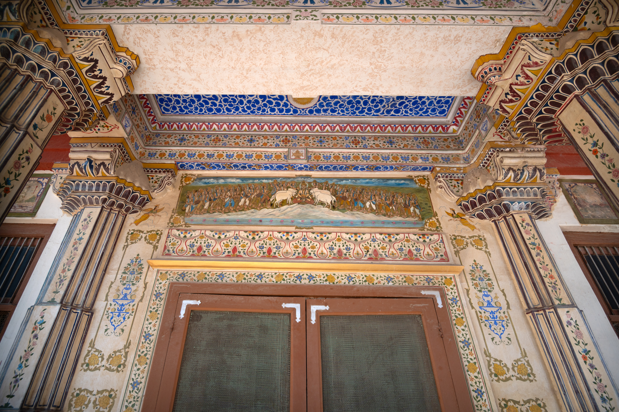 The main doorway that leads to the Bhandasar Temple is decked with various paintings. The pillars are painted white, while the Bengal arch roof is painted blue. There is a painting of a Jain Tirthankara on the rectangular slab above the doorway.