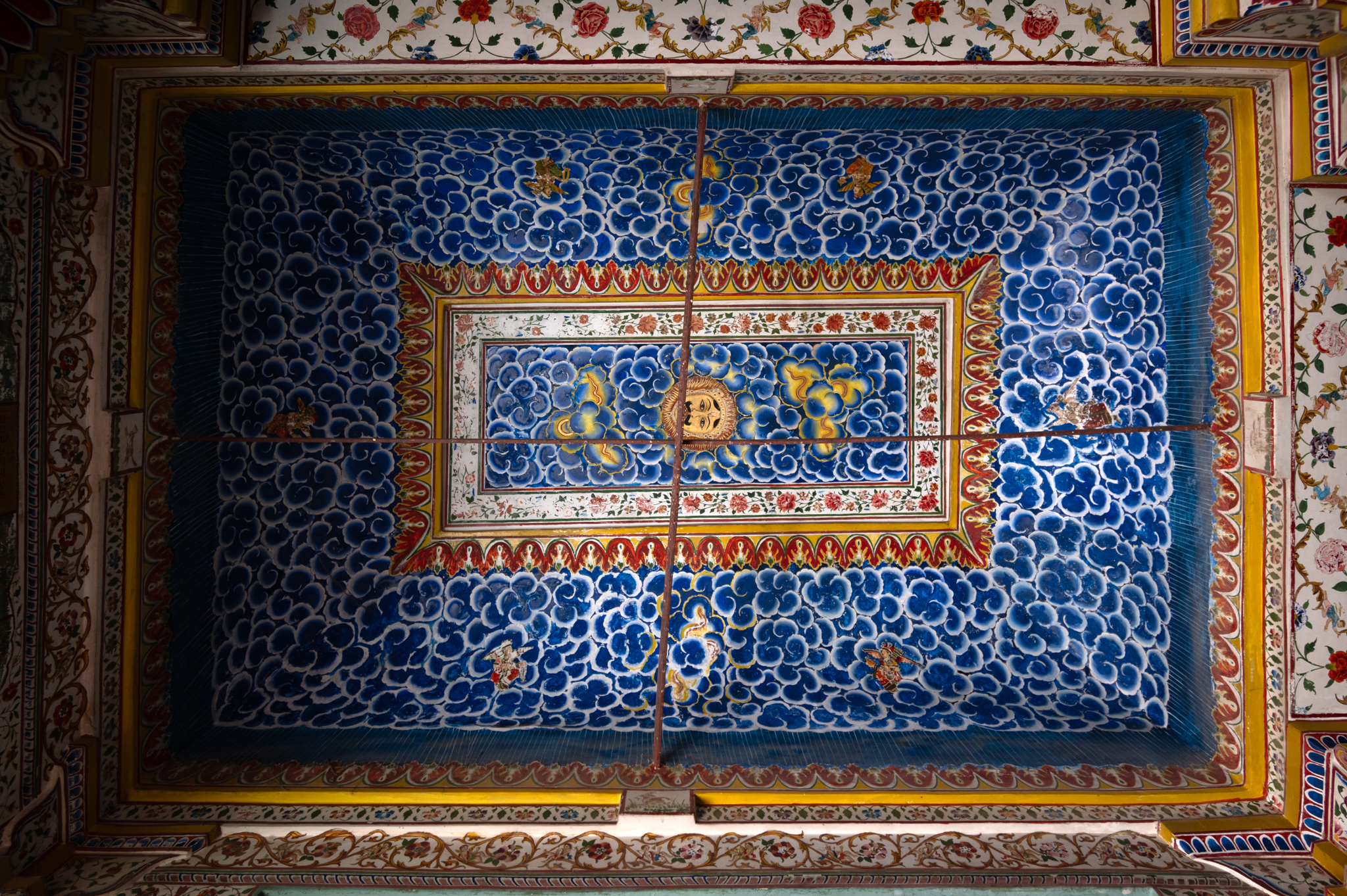 The aisles of the mandapa (pillared hall) of the Bhandasar Temple have a curved arch ceiling with bands of floral motifs on the corner, and the rectangular portion is filled with blue cloud-like designs. In contrast to the multicoloured dome at the centre of the mandapa, this blue rectangular ceiling stands out.