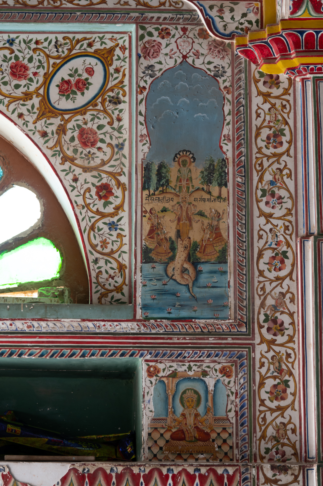 Painting of Parshvanatha Tirthankara on the wall flanking the side entrance doorways of the mandapa (pillared hall) of the Bhandasar Temple. Standing on a hooded snake, Parshvanatha is shown emerging from the mouth of the snake amidst water. He has four attendants on either side. The inscription reads– ‘megh malinapa sarga parshvanathji’.