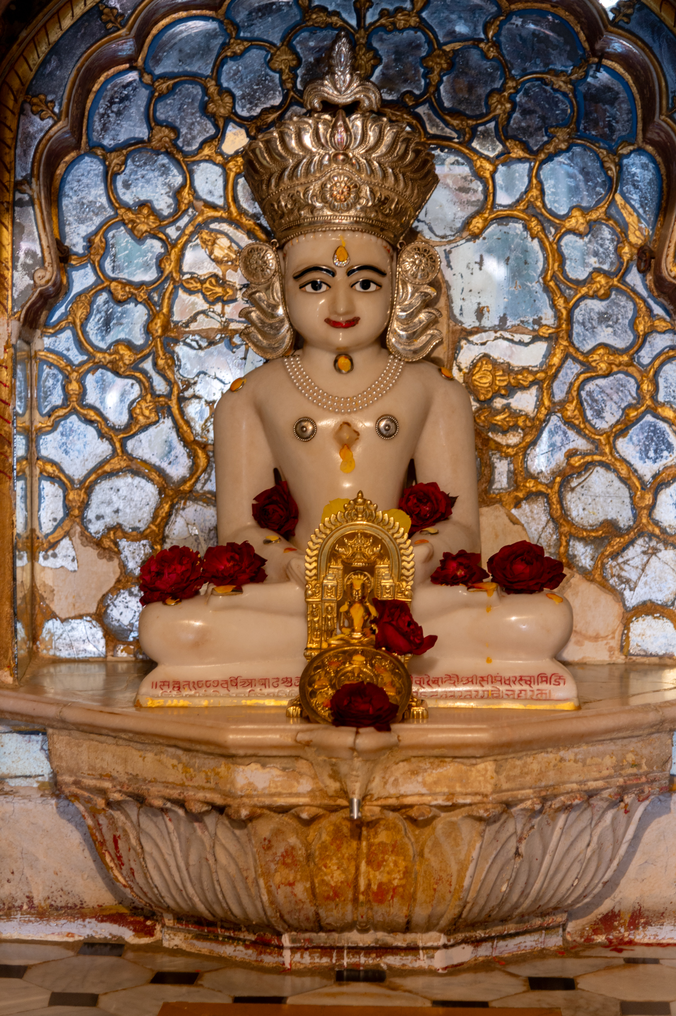 The enshrined white marble image, is probably of Rishabhnatha in the garbhagriha (sanctum sanctorum) of the Adinatha Temple. The Tirthankara, with a crown and elongated earlobes, is seated in padmasana (lotus pose) on a lotus pedestal. The base of the sculpture has an inscription incised with red colour.