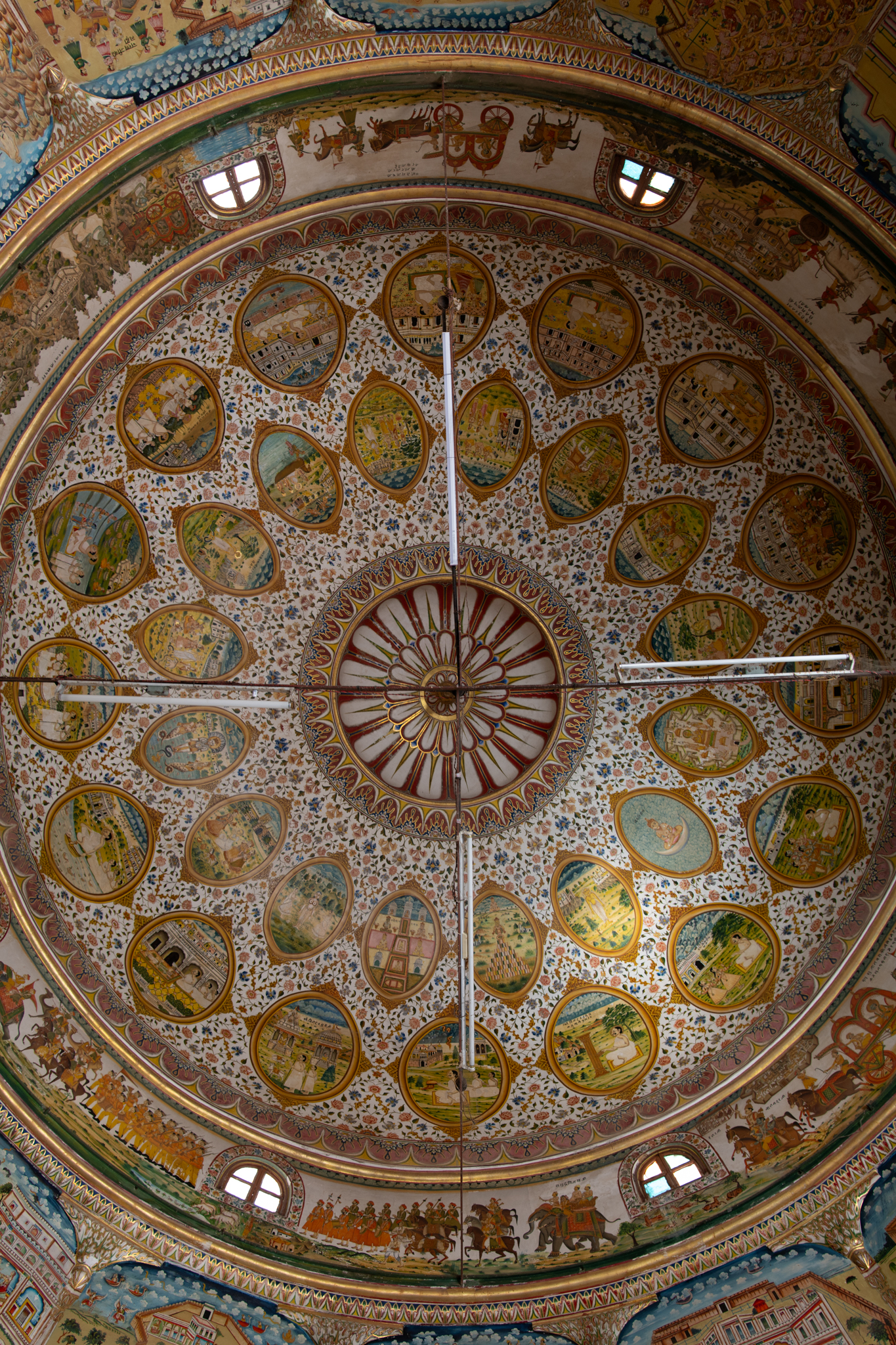 The dome above the mandapa (pillared hall) of the Bhandasar Temple features two circles consisting of sixteen oval-shaped designs resembling mirrors. The outer or lower row depicts miraculous deeds from the lives of Jain Acharyas, Dada Guru Jinadatta Suri and Dada Guru Jinachandra Suri. The inner or upper row has stories from the lives of Rishabhnatha, Mahavira, Parshvanatha and Neminatha Tirthankaras. This row also includes auspicious symbols and preachings of the Jain traditions. The oval paintings are placed on a background of floral ornamentation. All the paintings have inscriptions detailing the stories they represent.