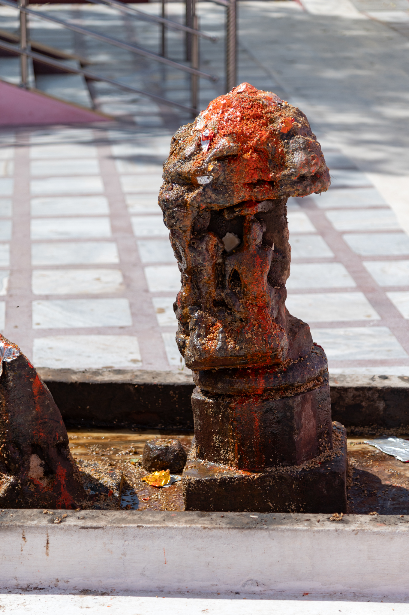 A pillar fragment with sculptures on its four sides, of which only two have survived. One image is of a seated Ganesha with four hands, and another is a seated male figure. The finial of the pillar fragment is shaped like a phamasana (pyramidical type) of shikhara (superstructure or spire). The spire has gavaksha (dormer window) motifs on the sides.