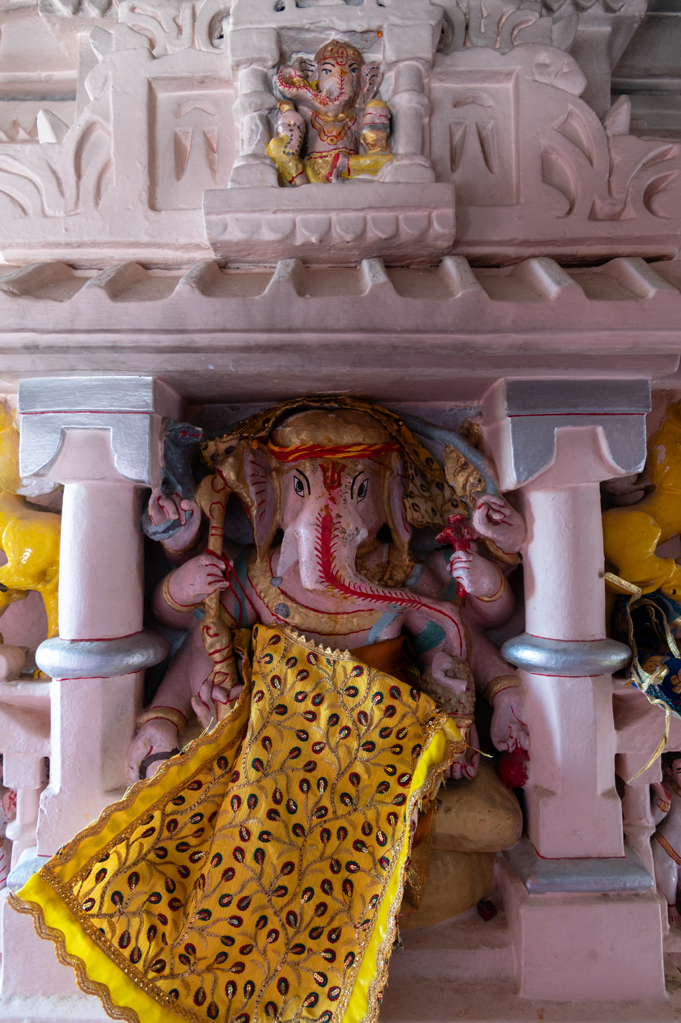 Ganesha sculpture in the devakoshtha (niche) on the bhadra (principal or central projection) of the south-facing wall of Suswani Mata Temple. Framed in a niche composed of two pilaster motifs surmounted by a pediment of gavasksha (dormer window) designs, the main Ganesha image is supported by another small Ganesha in a small frame right above its head. It is a seated, eight-handed image of Ganesha. Some of the visible attributes of the image are pasha (noose), ankush (bullhook), sarpa (serpent) and bijapuraka (citron, symbolized as ‘seed of universe’).