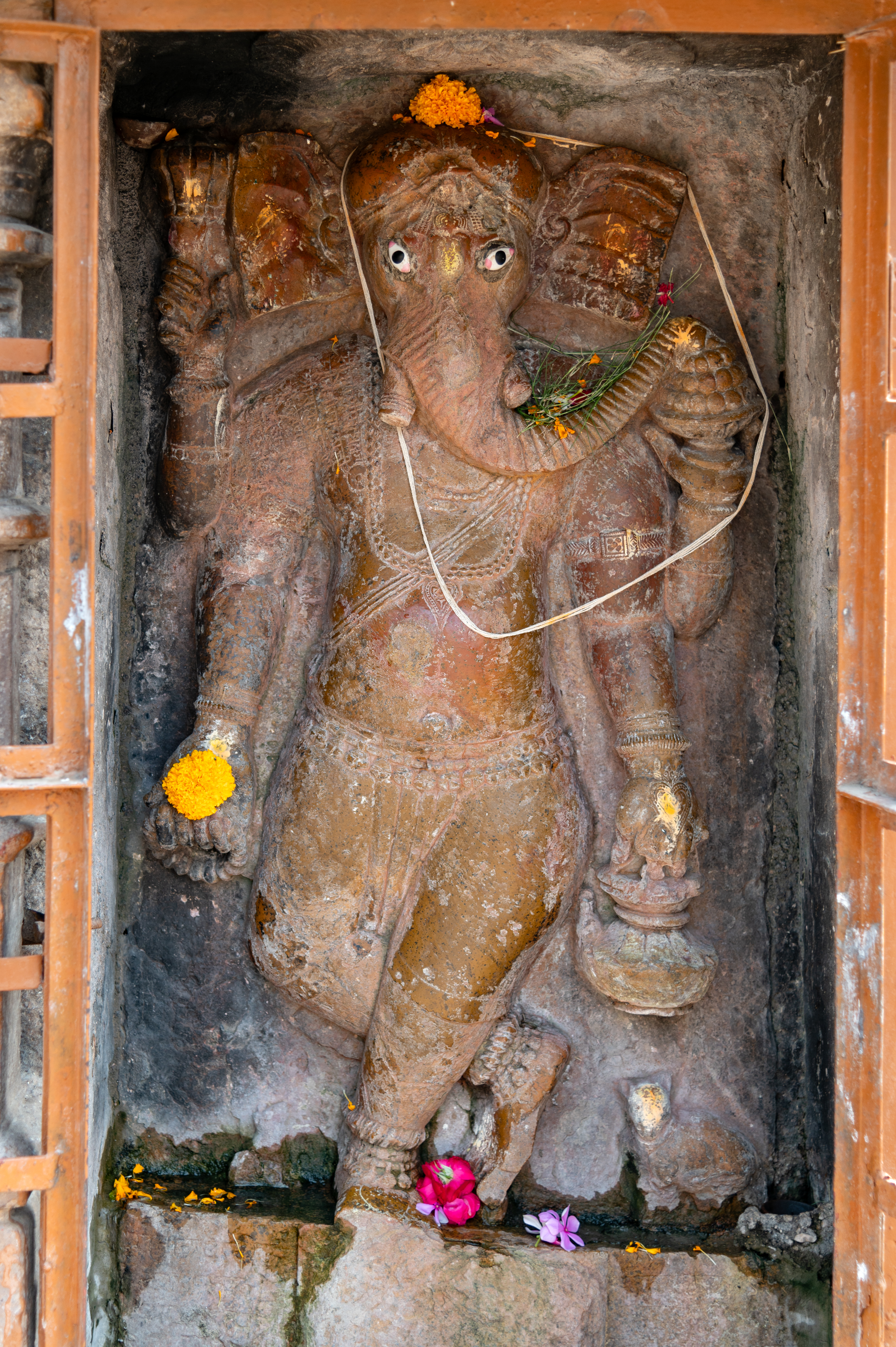 To the left of the mukhamandapa (front porch) of the Mahakal Temple, one can observe a standing statue of Ganesha. This depiction shows him with four arms, carrying a kamandalu (water pot), akshmala (rosary), another object and a bowl filled with modaks (a form of sweet with stuffing).