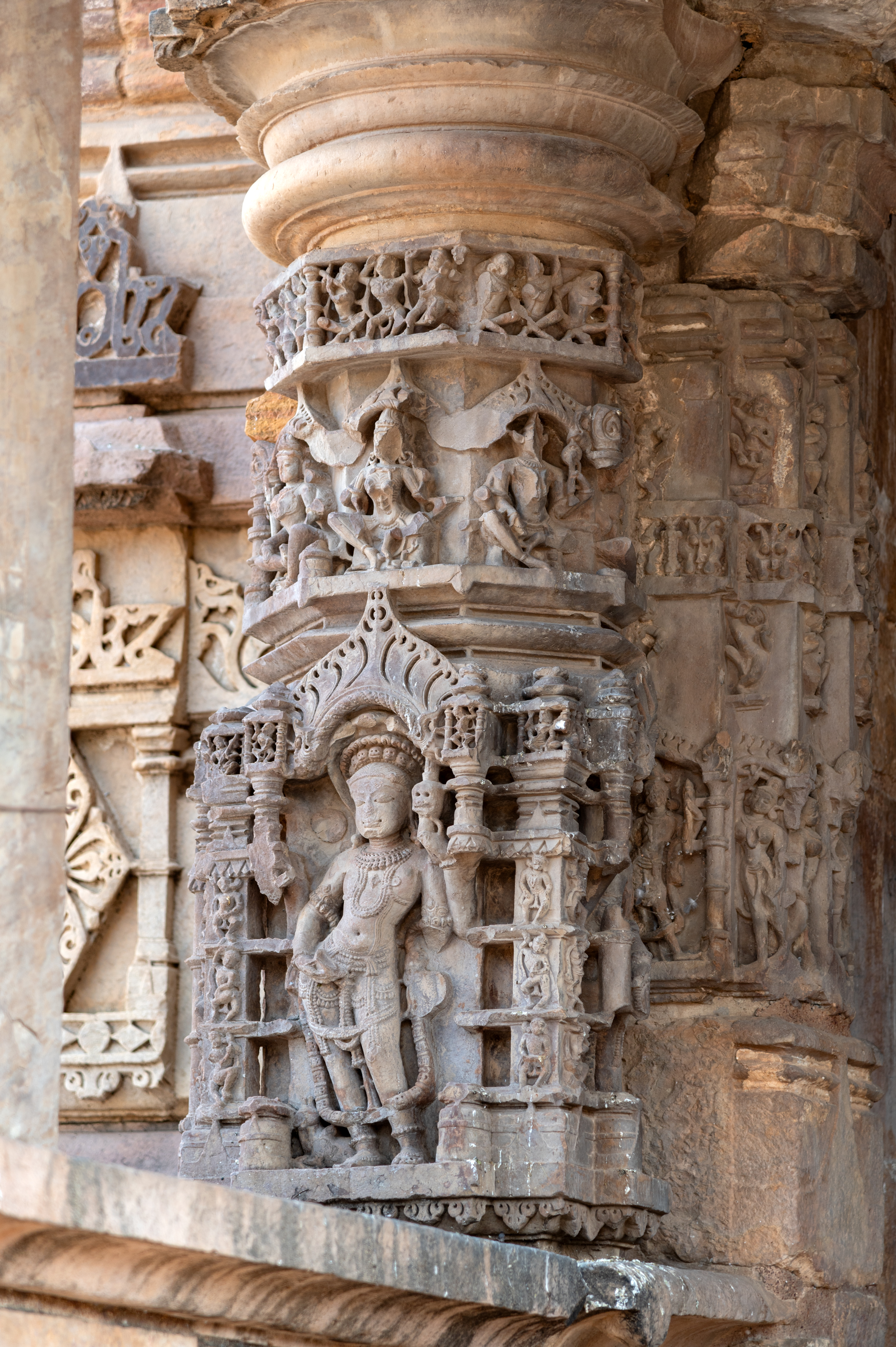 The mukhamandapa (front porch) of the Mahakal Temple serves as a narrow corridor flanked by kakshasanas (seat backs) on either side, with four pillars supporting its flat roof. These pillars have square bases intricately carved with divine figures on all four sides. The upper section adopts an octagonal shape, embellished with miniature niches on all sides housing seated goddess figures. Crowning this, there's a band adorned with various figures and a kirtimukha (face of glory) motif.