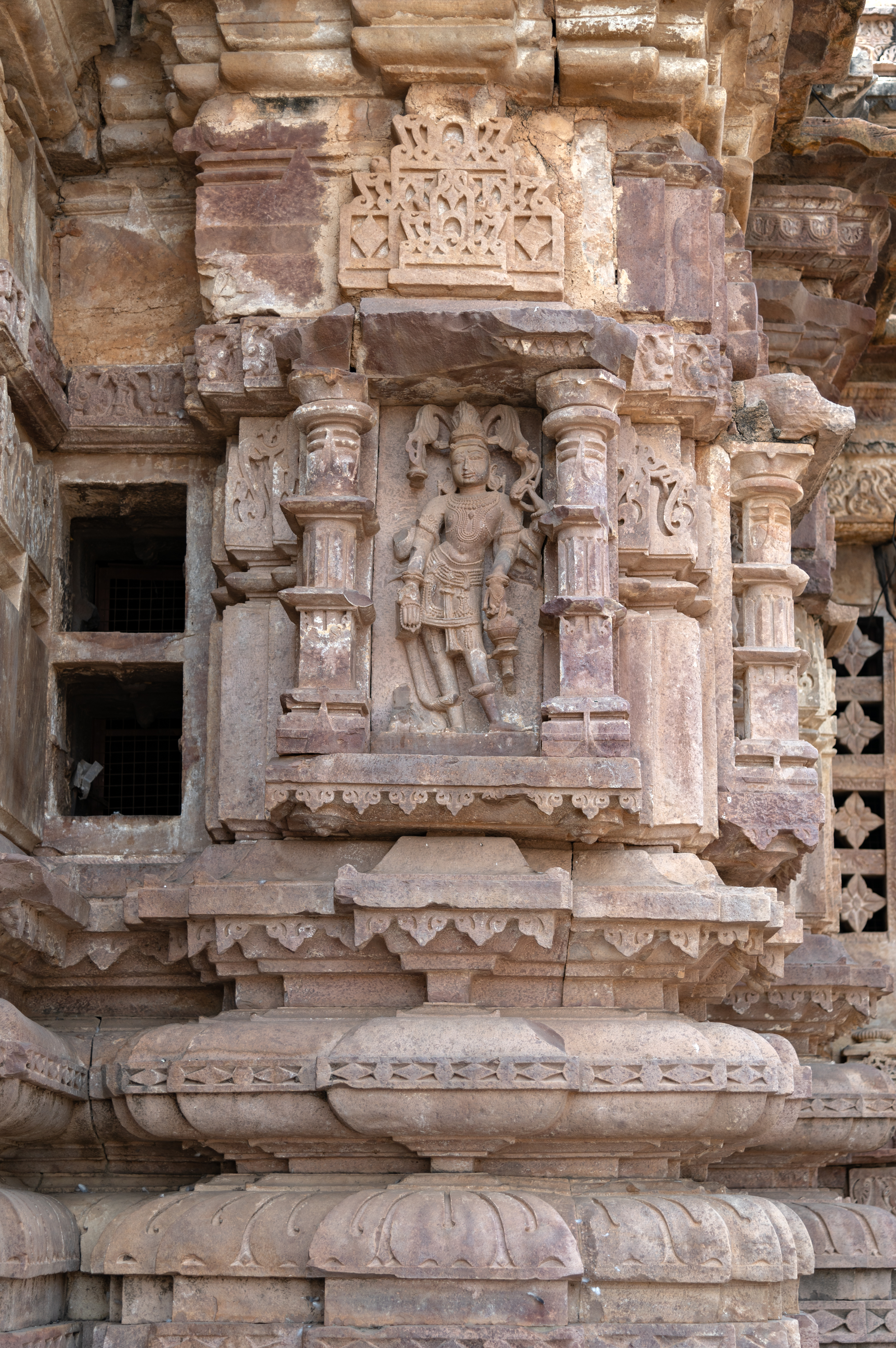 On the opposite side of Kubera, Ishana is depicted, holding a trishula (trident) in his upper right hand, albeit now damaged. His upper left hand grasps a sarpa (serpant), while his lower left hand holds a kamandalu (water pot). Positioned in varada hasta (hand gesture of conferring a boon), his lower right hand carries a rosary. At the bottom, a bull was originally carved, though it's now broken.