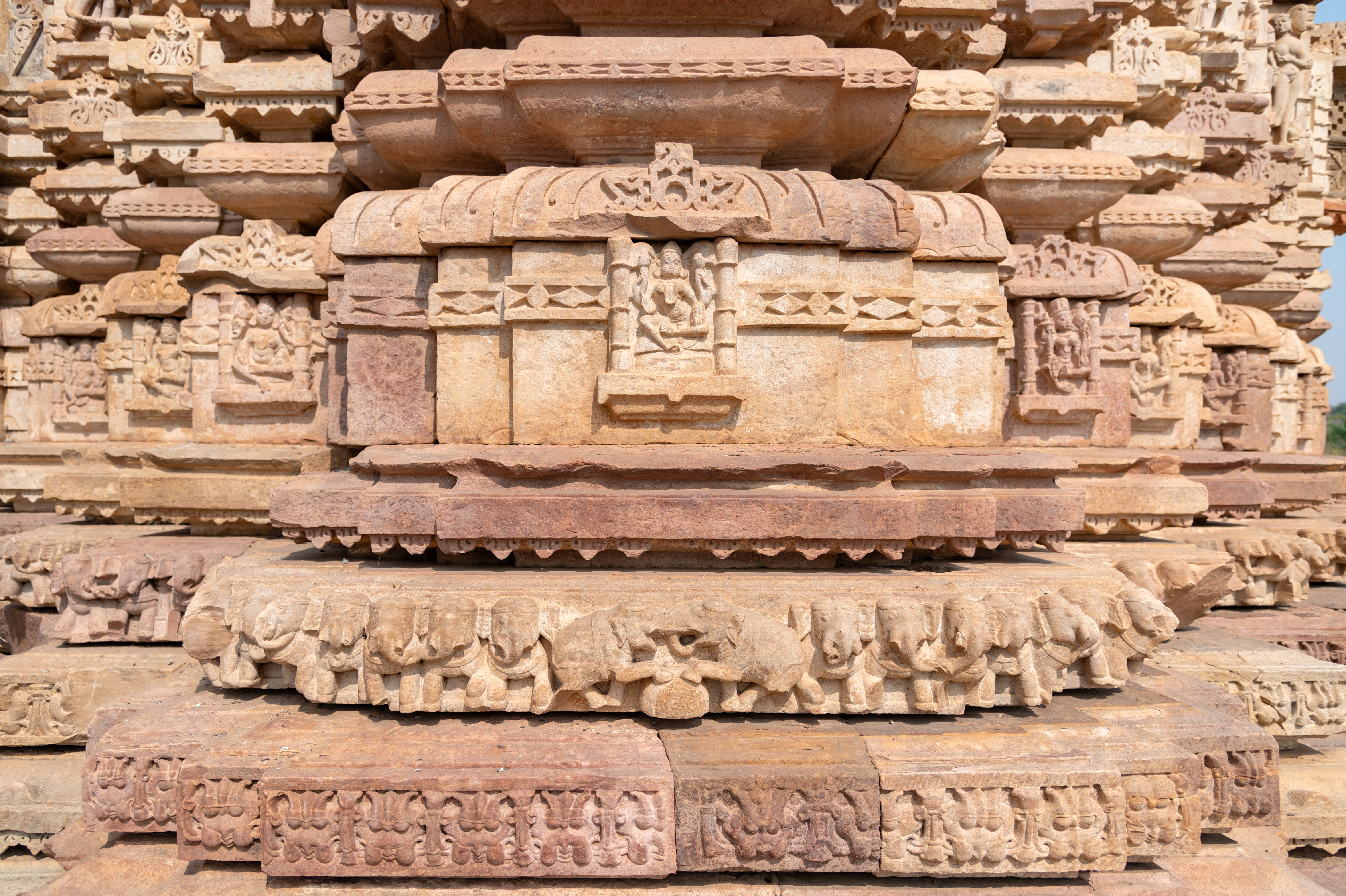 The closer view of the vedibandha (basal mouldings) of the Undeshwar Temple shows the gajathara moulding (elephants in the band). This moulding is commonly found in grand Bhumija temples. The kumbha (pot) moulding is adorned with miniature niches containing figures of deities. The kalasha (pitcher) moulding is also intricately carved with a band featuring a diamond motif.