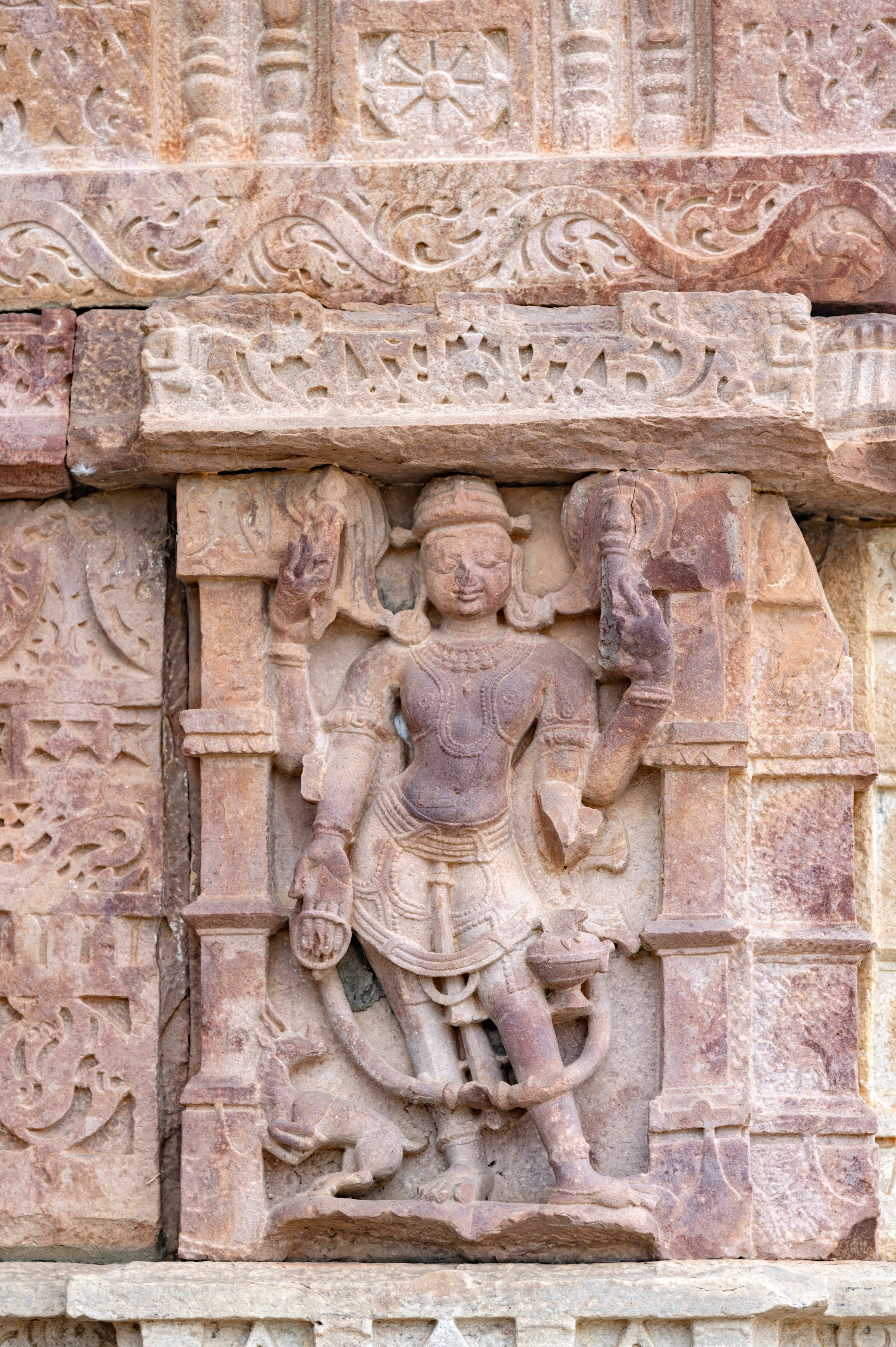 The opposite side of the niche, of the kakshasana (seat back) of the Undeshwar Temple, portraying Varuna features Vayu. Vayu is depicted as a tall, smiling figure with four arms, shown standing. He holds a staff in his upper hands, while a kamandalu (water pot) and a gesture of varadaksha (of blessing) are depicted in his lower hands. At the bottom of the niche, Vayu's vehicle, the antelope, is depicted in motion.