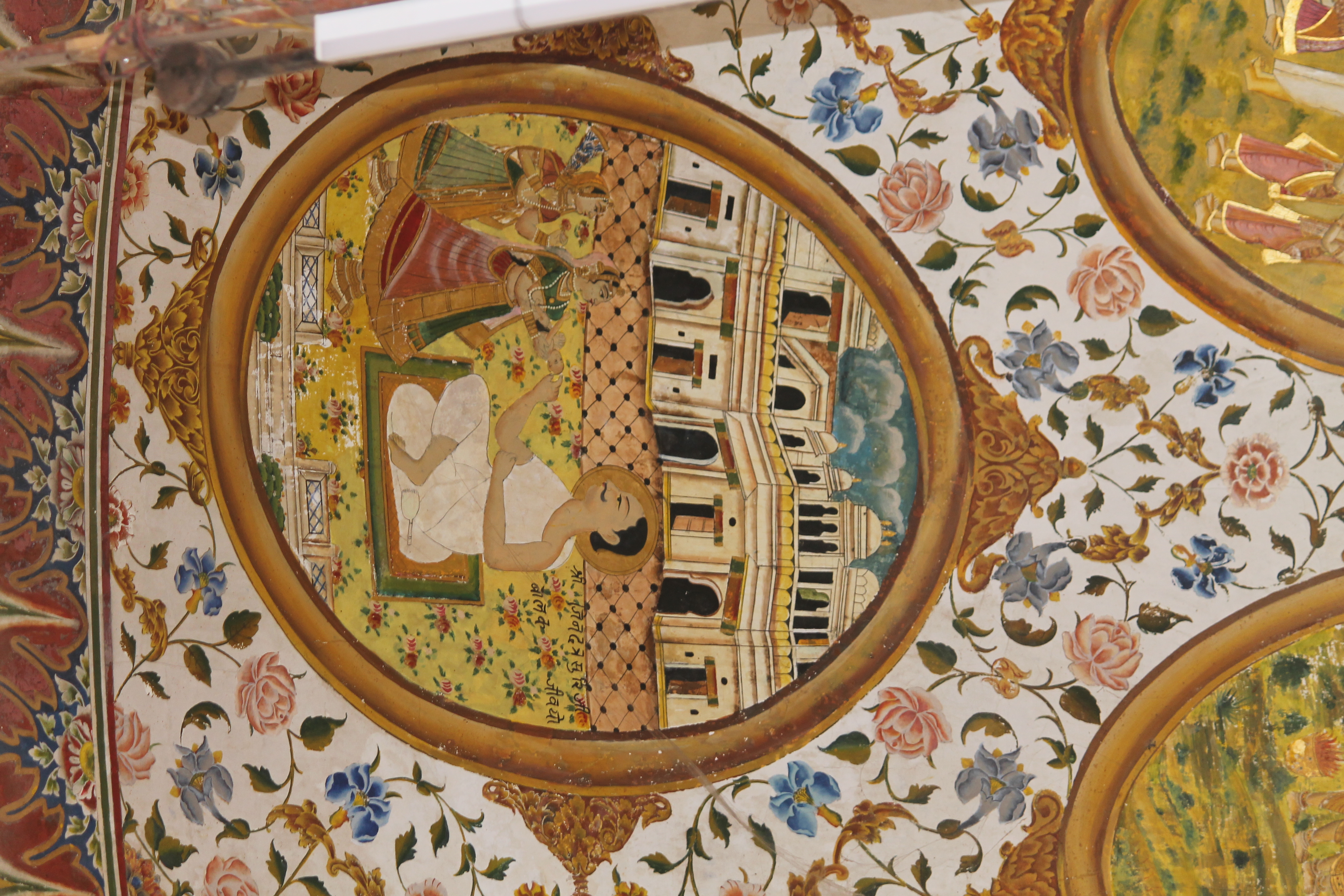 The fifth oval painting (in clockwise order) in the lower/outer circle in the ceiling of the mandapa (pillared hall) is the episode where Jinadatta Suri saved the life of an unwell child brought to him by two women. The episode takes place outside a haveli, probably near the place where the acharya (those who impart knowledge) is meditating. The acharya is shown blessing the child by placing his palm on the child’s head. The inscription reads, ‘Shri Jinadatta Suriji balak jivayo.’