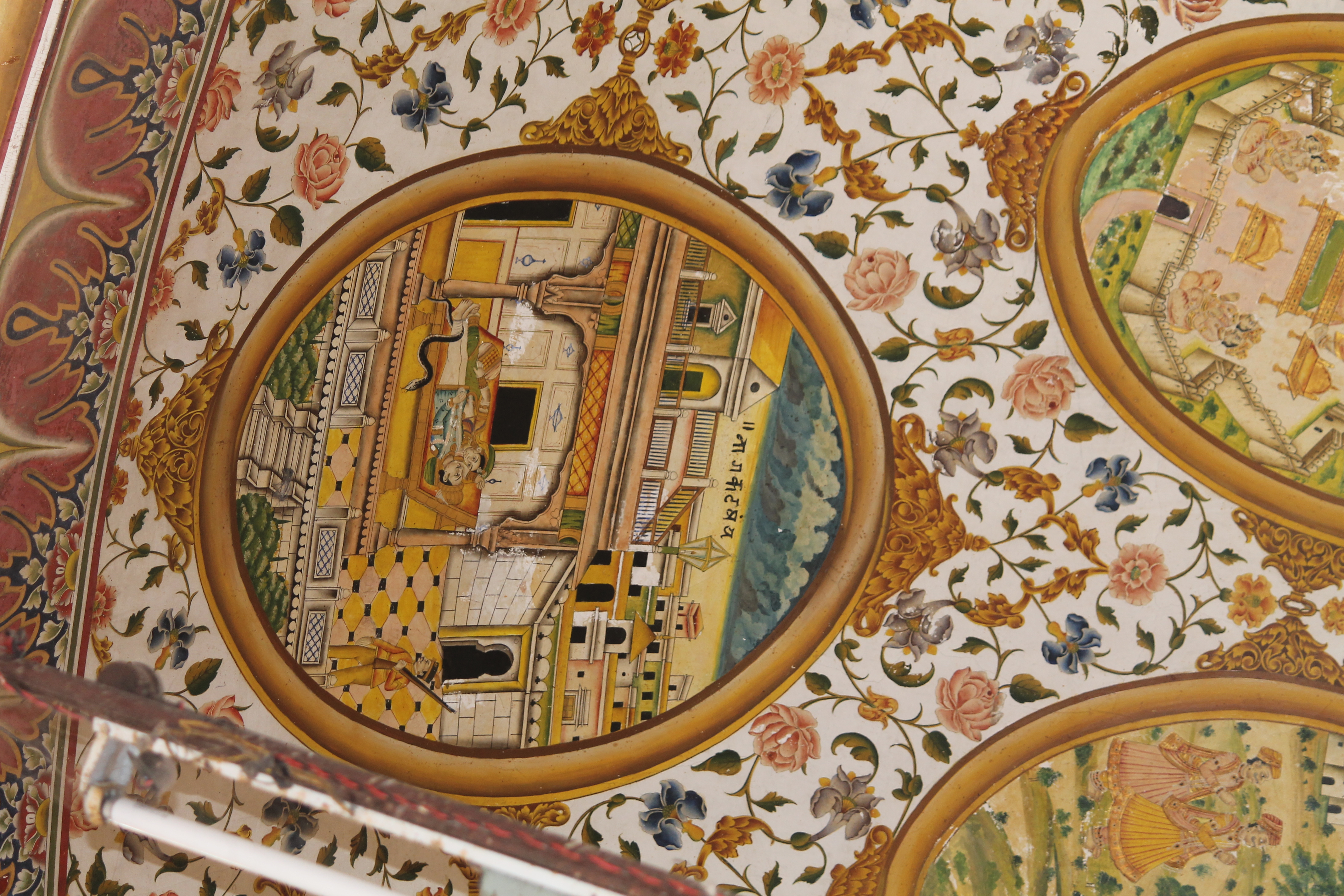 The ninth oval painting (in clockwise order) in the lower/outer circle in the ceiling of the mandapa (pillared hall) is difficult to decipher. It appears to depict a sleeping couple with a snake near the leg of the man. Outside the haveli (mansion), which houses this couple, there is an armed figure that looks like a soldier or guard in uniform.