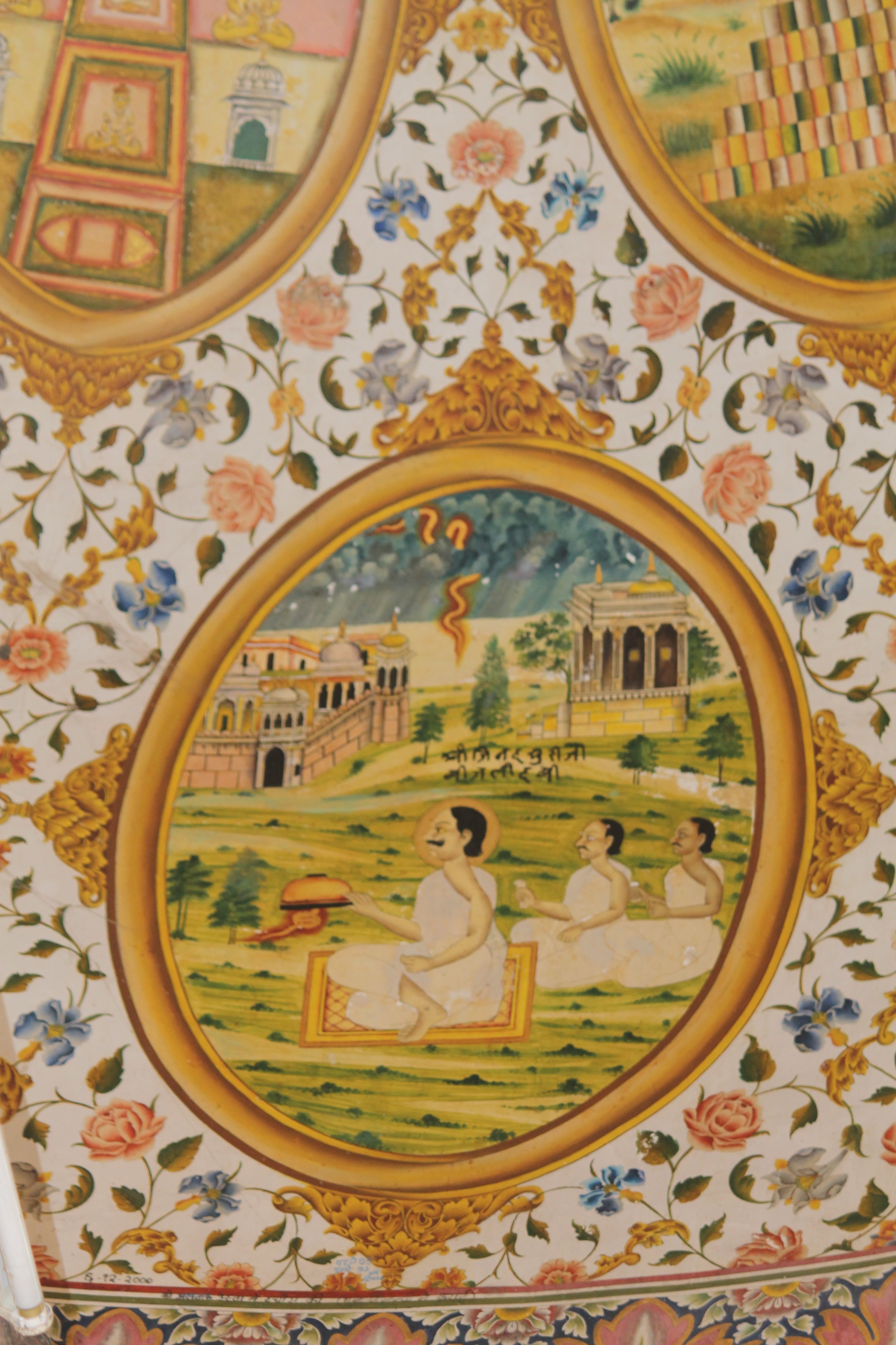 The thirteenth oval painting (in clockwise order) in the lower/outer circle in the ceiling of the mandapa (pillared hall) is the episode from Jinadatta Suri's life that took place in Ajmer. Once, an ominous stroke of lightning in the evening threatened the fellow monks and followers of Dada Jinadatta Suri while they were performing pratikraman with him. Dada Jindatta Suri captured the lightning under his alms bowl and instructed everyone to continue with the pratikraman without fear. Lightning is shown as yellow strokes in the sky that the acharya (those who impart knowledge) collected in the bowl. Jinadatta Suri is shown sitting on a mat. The inscription reads, ‘Shri Jinadatta Suri ji Bijali dabi.'