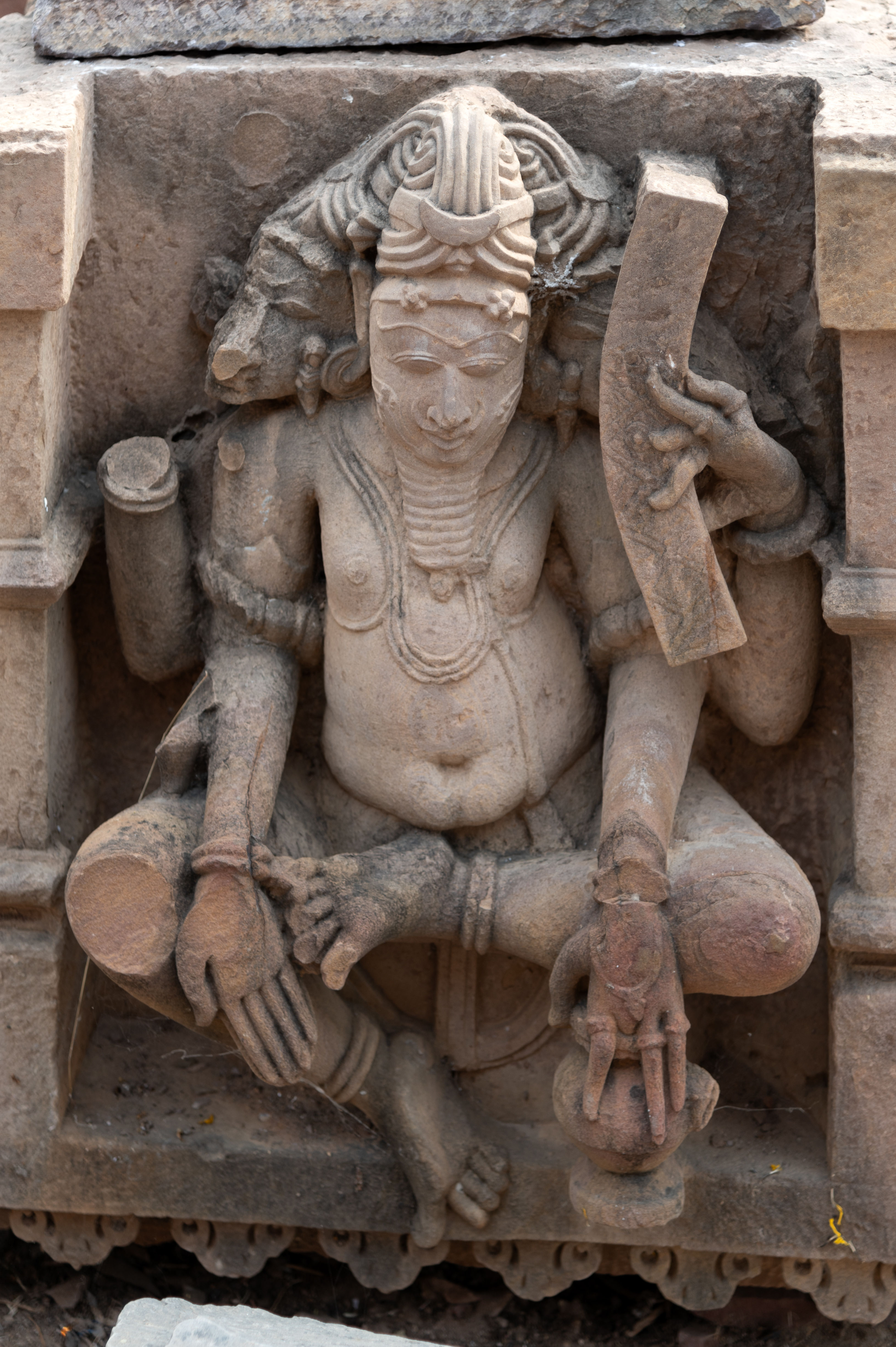 In the premises of the Mahanaleshwar temple complex, a loose sculpture of Brahma lies next to the pratoli (entrance gateway). The sculpture depicts a three-faced, four-handed, seated figure of Brahma, holding a pustaka (book) in the upper left hand and a kamandalu (sacrificial pot) in the lower left, with the attributes in the right hand missing. A niche houses a bearded potbellied figure with a jatamukuta (crown of mattered hair).