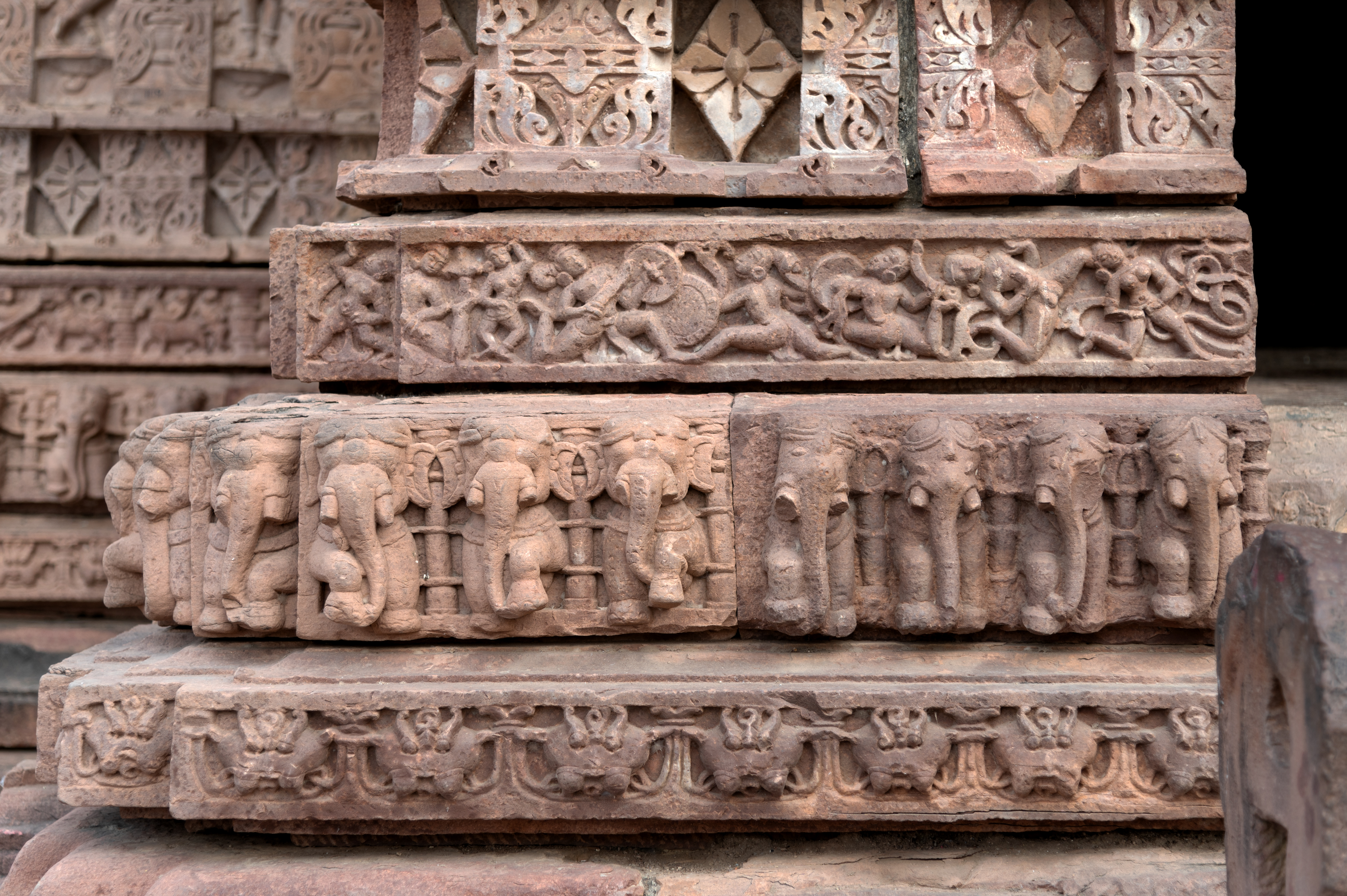 These are the plinth details of the east-facing elevation of the Mahanaleshwar Temple. Starting from the bottom to the top, there are four mouldings in the plinth, which consist of a plain kani moulding, graaspatti (a band of kirtimukha, or face of glory), gajathara (band of elephants), and narathara (moulding containing human figures). The narathara depicts mithuna (amorous couples), maithuna, and deities.