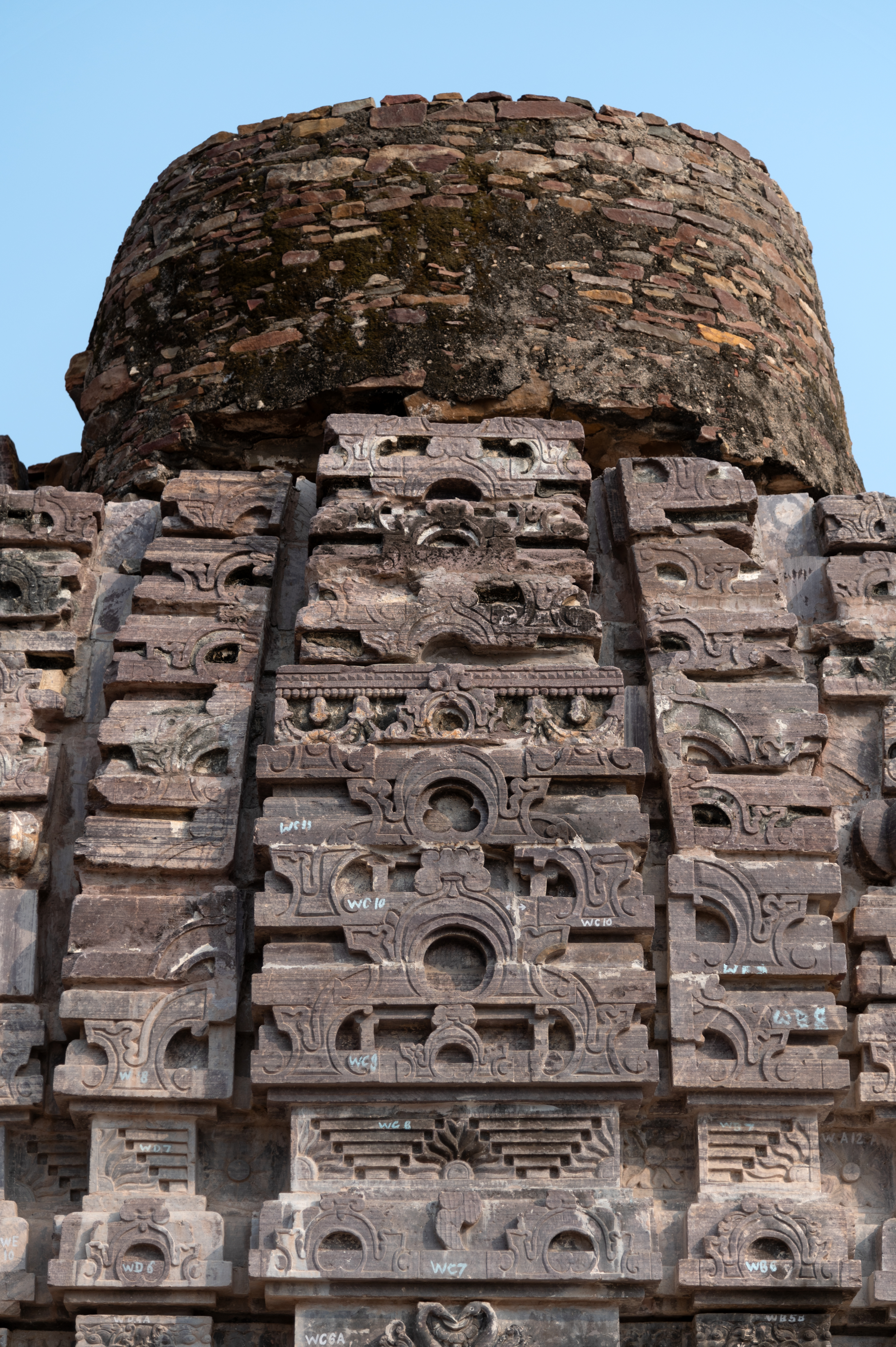 Seen here are the details of the latina shikhara (mono-spire superstructure) of the side shrine from the Triple-shrine Temple. The madhyalata (central band), a broad band, comprises a mesh of gavaksha (chaitya dormer motifs) arranged in ascending order. As the shikhara tapers upwards, the chaitya dormer motifs diminish in size. Protruding moulding and a decorative recess also form the base of the shikhara. The bands flanking the madhyalata are thinner and made up of half the designs of the chaitya dormer.