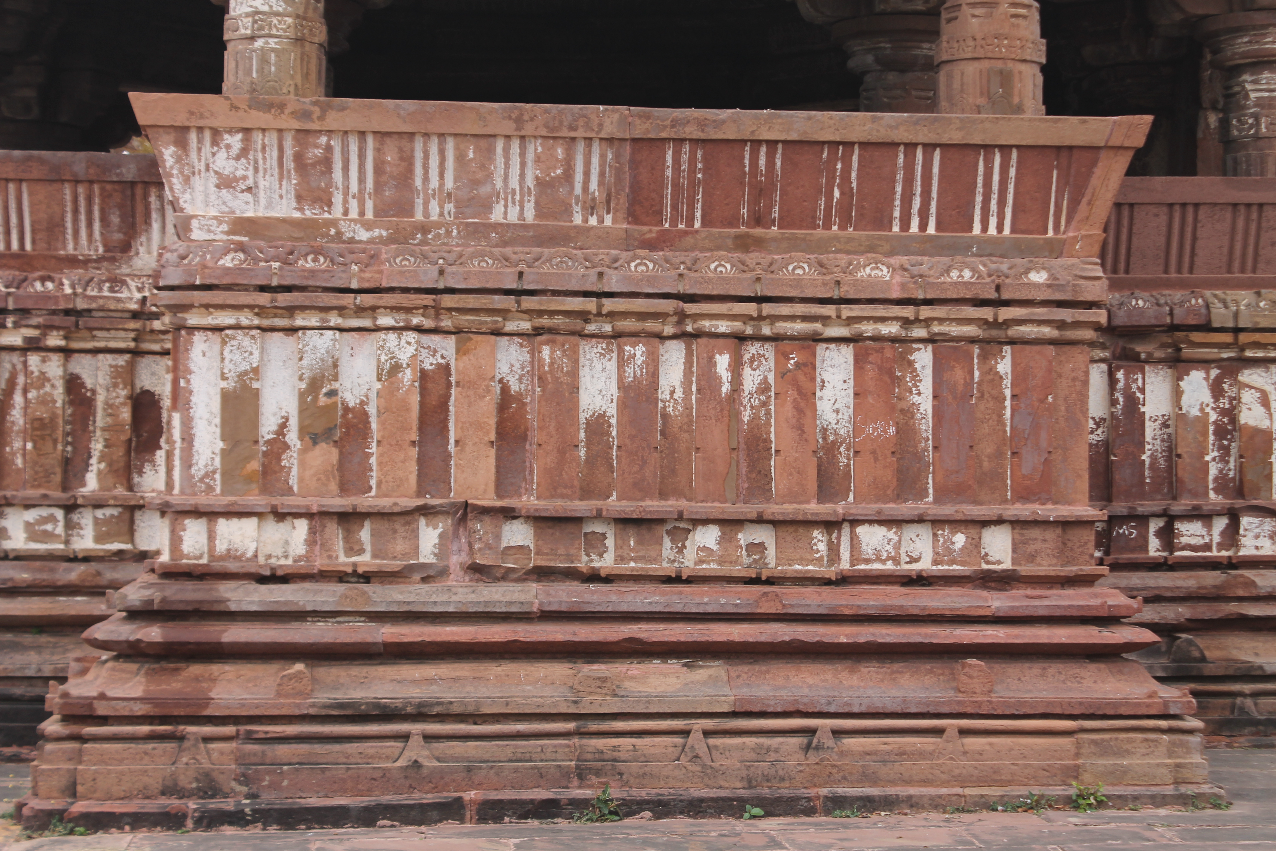 A view of the south elevation of the Suhaveshwar Temple's mandapa (pillared hall) is shown here. The mandapa has two lateral transepts on the north and south sides. The exterior of the transepts has plinth mouldings that support a plain wall that is ornamented with pilaster motifs. The dwarf walls are adorned with slender and slanting kakshasana (seat backs) featuring balustrade designs. Both the vedika (wall) and the kakshasana's slanting seat back are devoid of ornamentation patterns.
