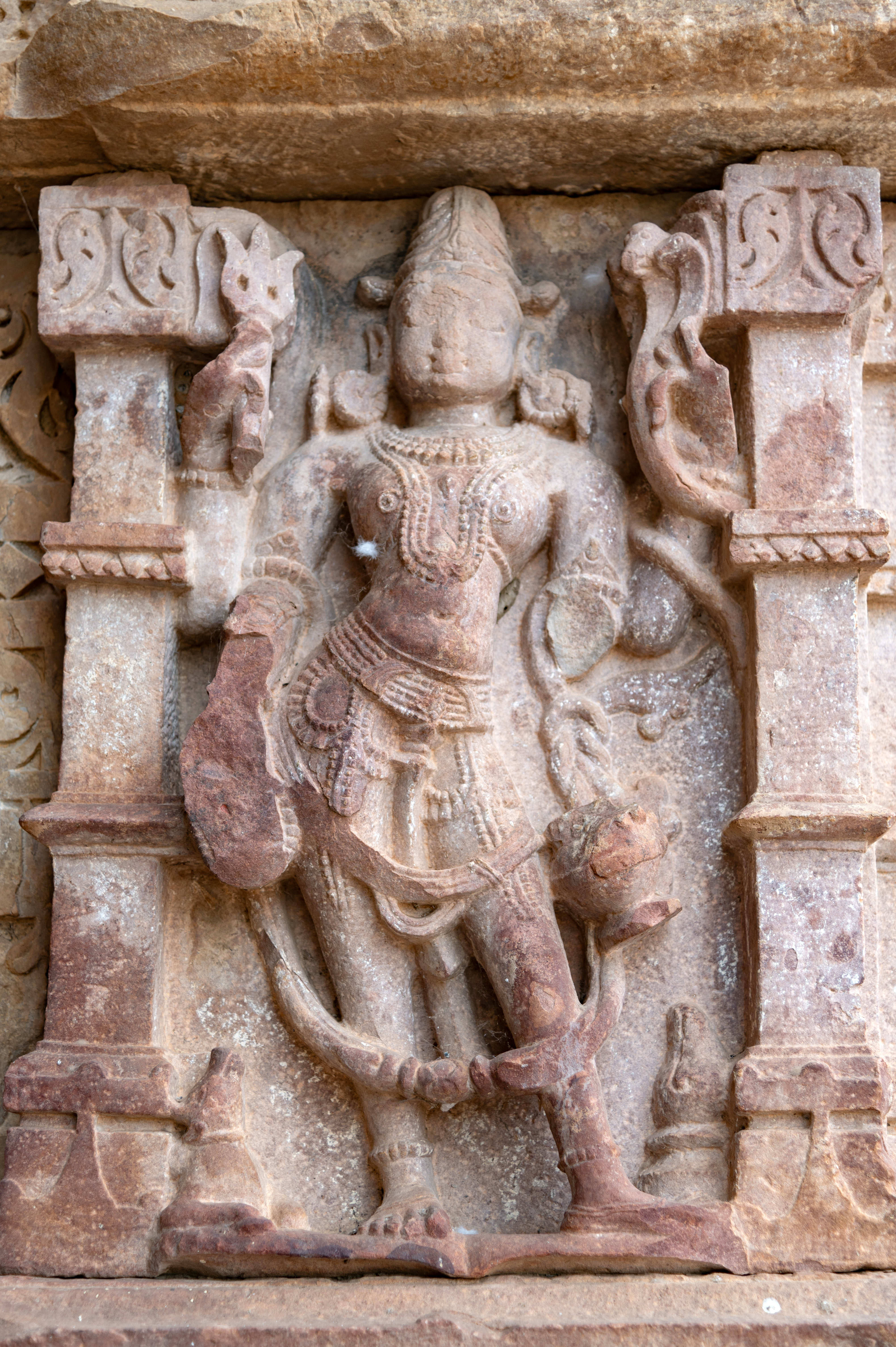 Ishana is depicted with four arms, holding a trishula (trident) and sarpa (snake) in his upper hand. He is holding a kamandalu (water pot) and varadaksha in his lower hands. He wears a jatamukuta (crown of matted hair) and is adorned with jewels. At the bottom right, his mount, the bull, is carved.