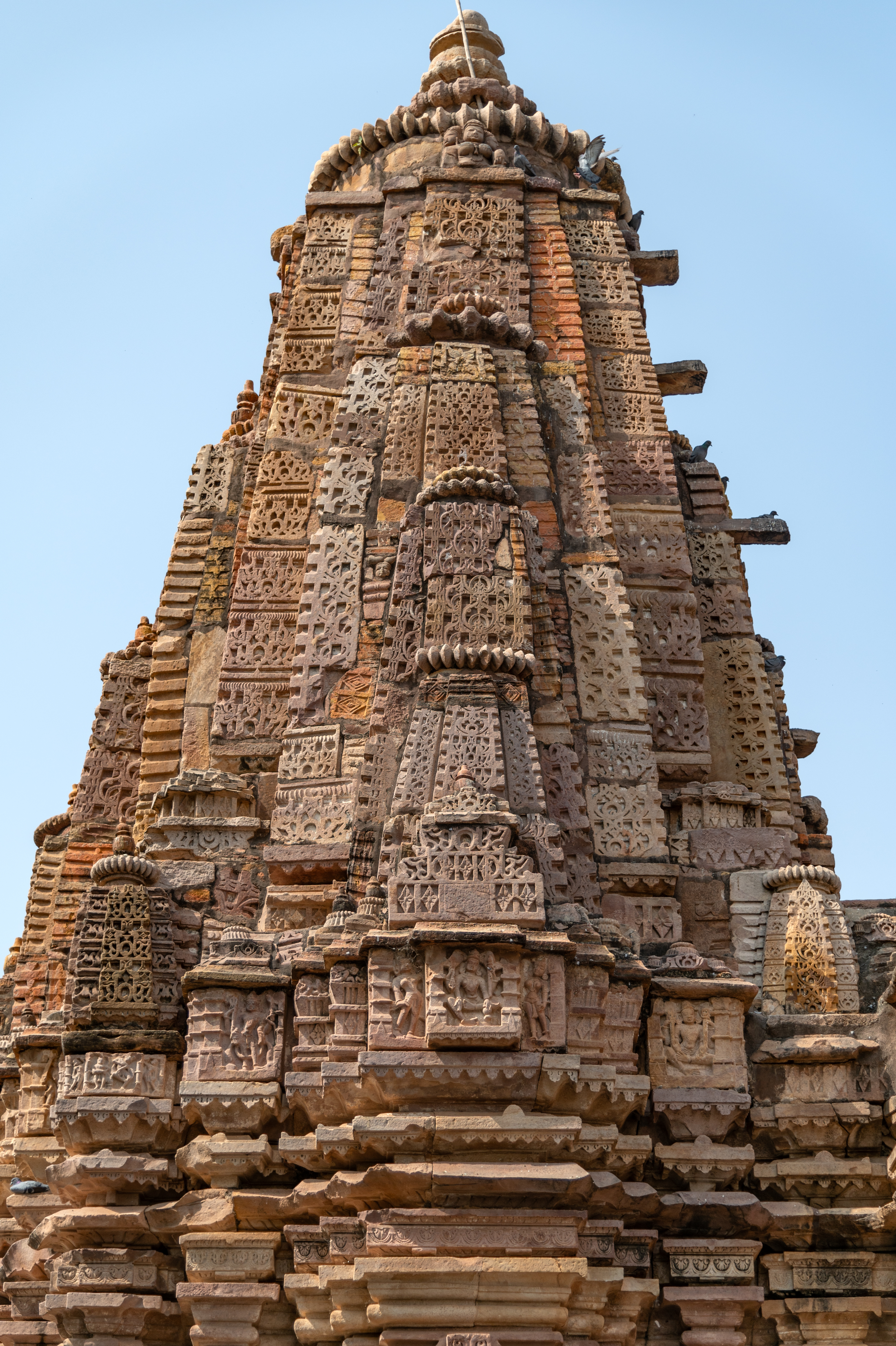 Image 24: The shikhara (superstructure) stands as a fusion of architectural elements, where a towering vertical spire intertwines with the half spires and the miniature spires. The central offset is embellished with the surasenaka (pediment made of chaitya dormer), crowned by a kirtimukha (face of glory) at its zenith.