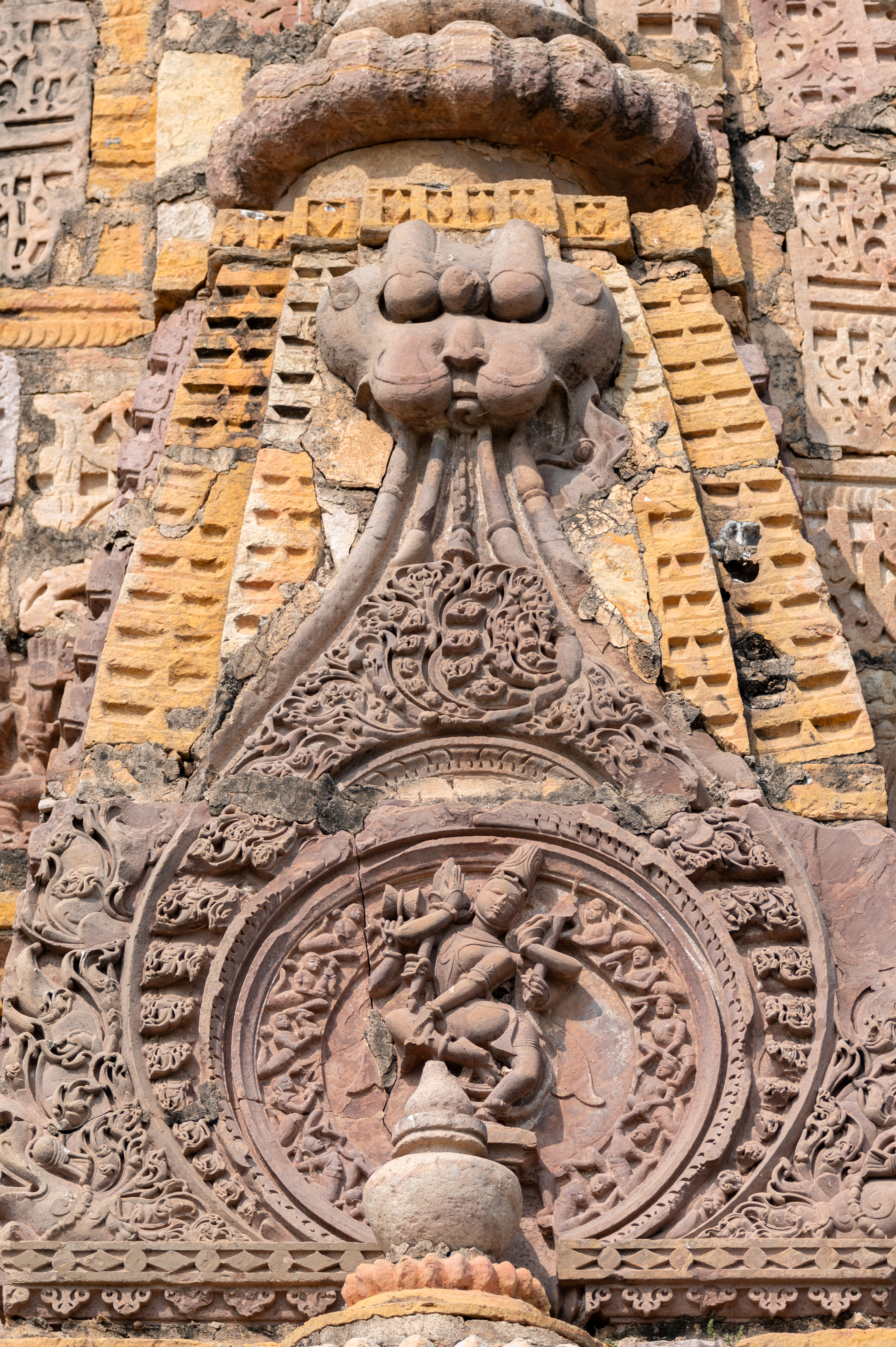 Image 27: One of the surasenakas (pediment made of chaitya dormer) features a sculpture capturing the divine dance of Shiva. From the rear, Shiva’s upper body twists towards the front, conveying dynamic movement and cosmic rhythm. Though some of his arms are now broken, remnants of divine attributes are visible, including a damru (drum) symbolizing the rhythm of creation and other sacred objects. One of his arms extends in the gajahasta gesture, resembling an elephant trunk. He has a jatamukuta (crown of matted hair), a moustache and a beard, and he is surrounded by celestial gandharvas (celestial musicians). This sculpture captures the timeless essence of Shiva’s cosmic dance, embodying the eternal flow of creation, preservation and destruction.