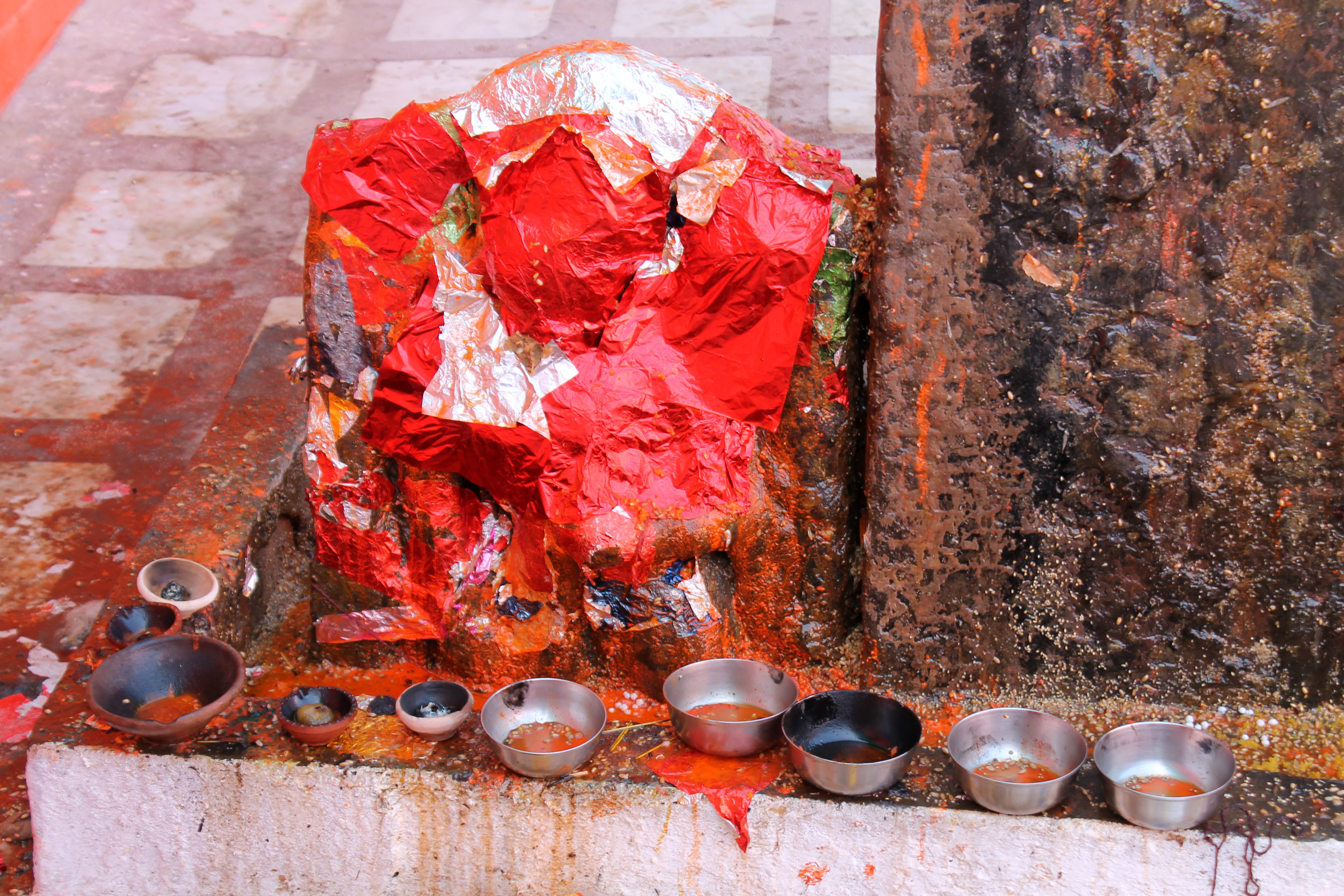 This is an unidentified fragment in the row of hero stones that are kept on the premises of Suswani Mata Temple. Today, the stone fragment is wrapped in a red paper sheet and revered by some as Ganesha. The original style and composition of the stone fragment are not known. The newly wrapped paper serves as an attempt to make them resemble Ganesha.