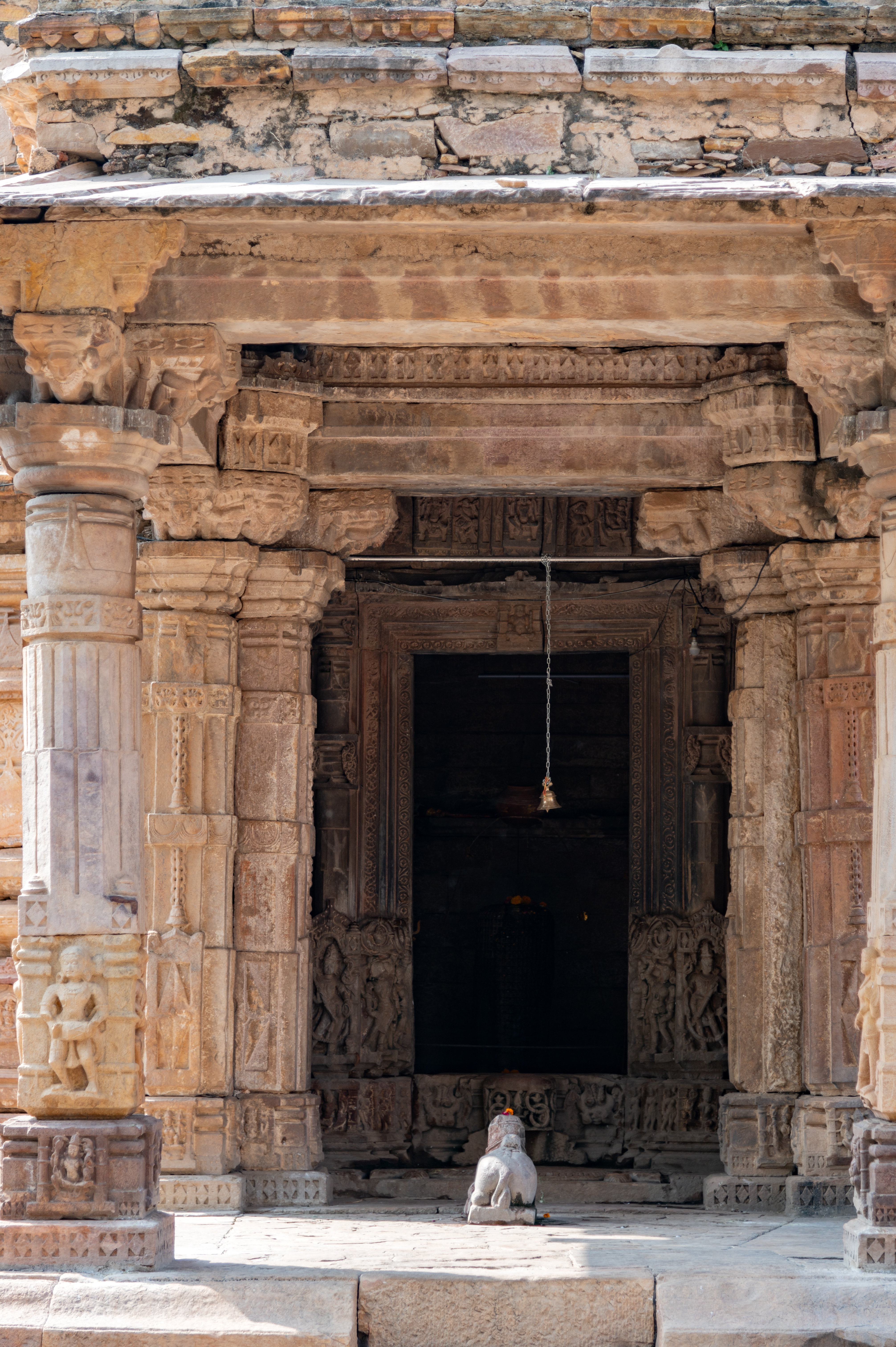 Image 14: The mandapa (pillared hall) of the Hazareshwar Temple is a small square open hall that stands on a low base, supported by four pillars positioned at its corners. These pillars feature square bases adorned with depictions of deities. The shaft of the pillars is intricately carved with male deities, musicians, dancers and surasundaris (celestial damsels). Transitioning into an octagonal shape, then into sixteen facets and circular, the shaft culminates with an abacus supporting bharavahaka (load bearers) brackets, which in turn uphold the lintel. The mandapa's ceiling, square in shape, is exquisitely carved. There is an idol of Nandi housed at the centre of the mandapa.