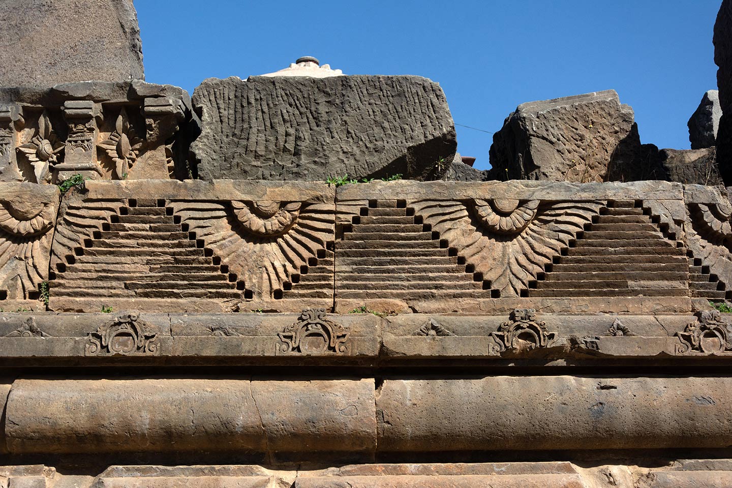 Broken debris from the original temple assembled on the south face of the adhisthana. Around the adhisthana, relief carvings of geometric, flora, and fauna motifs are visible.