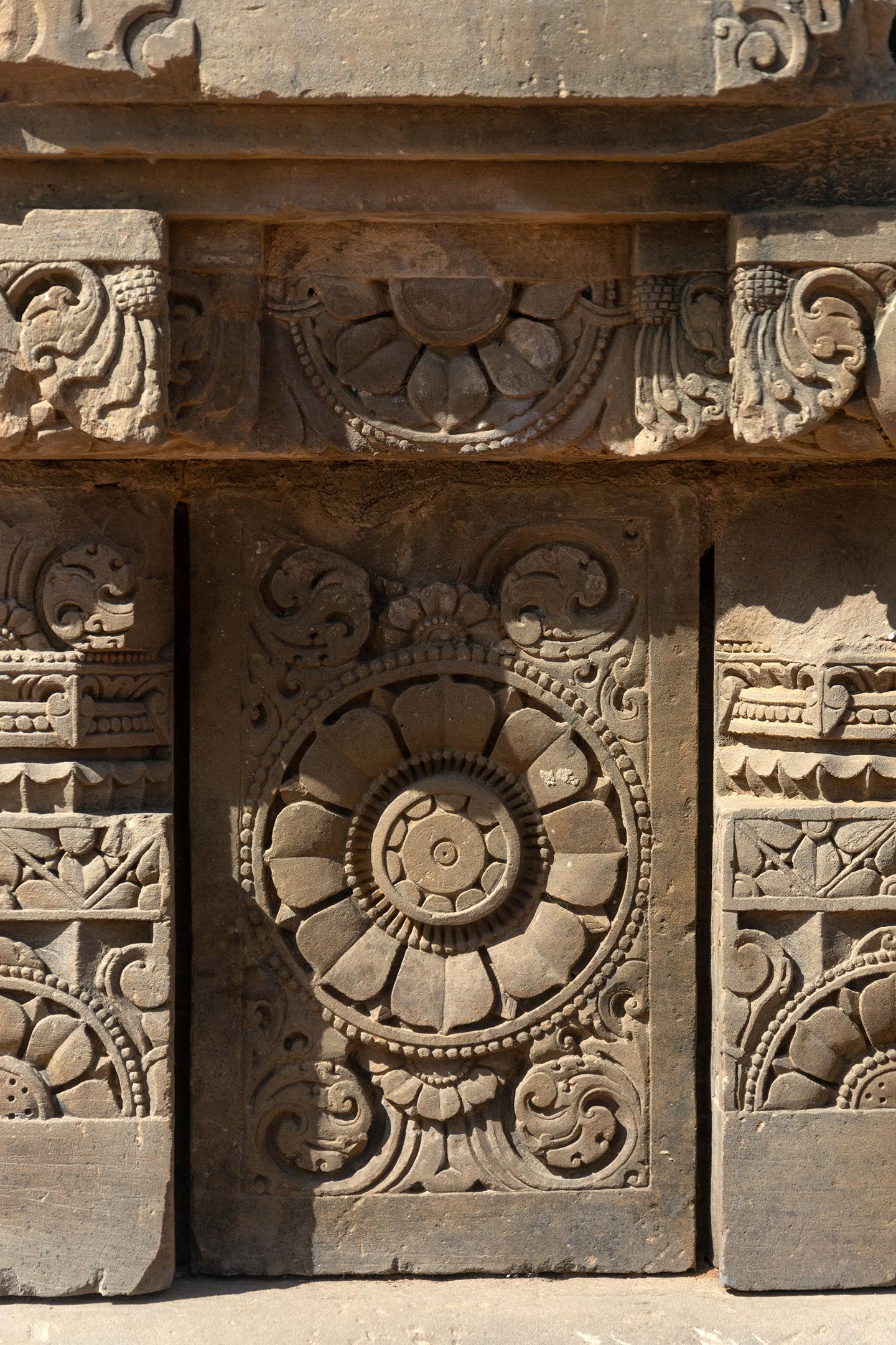 The ashtadal kamal (lotus with eight petals) is featured on the plaque. Squat pillars, characterized by a square base, an octagonal shaft, and a square capital, divide the plaques. The pillars are decorated with ardha padma (half lotus) and kalpa lata (creeper) motifs.