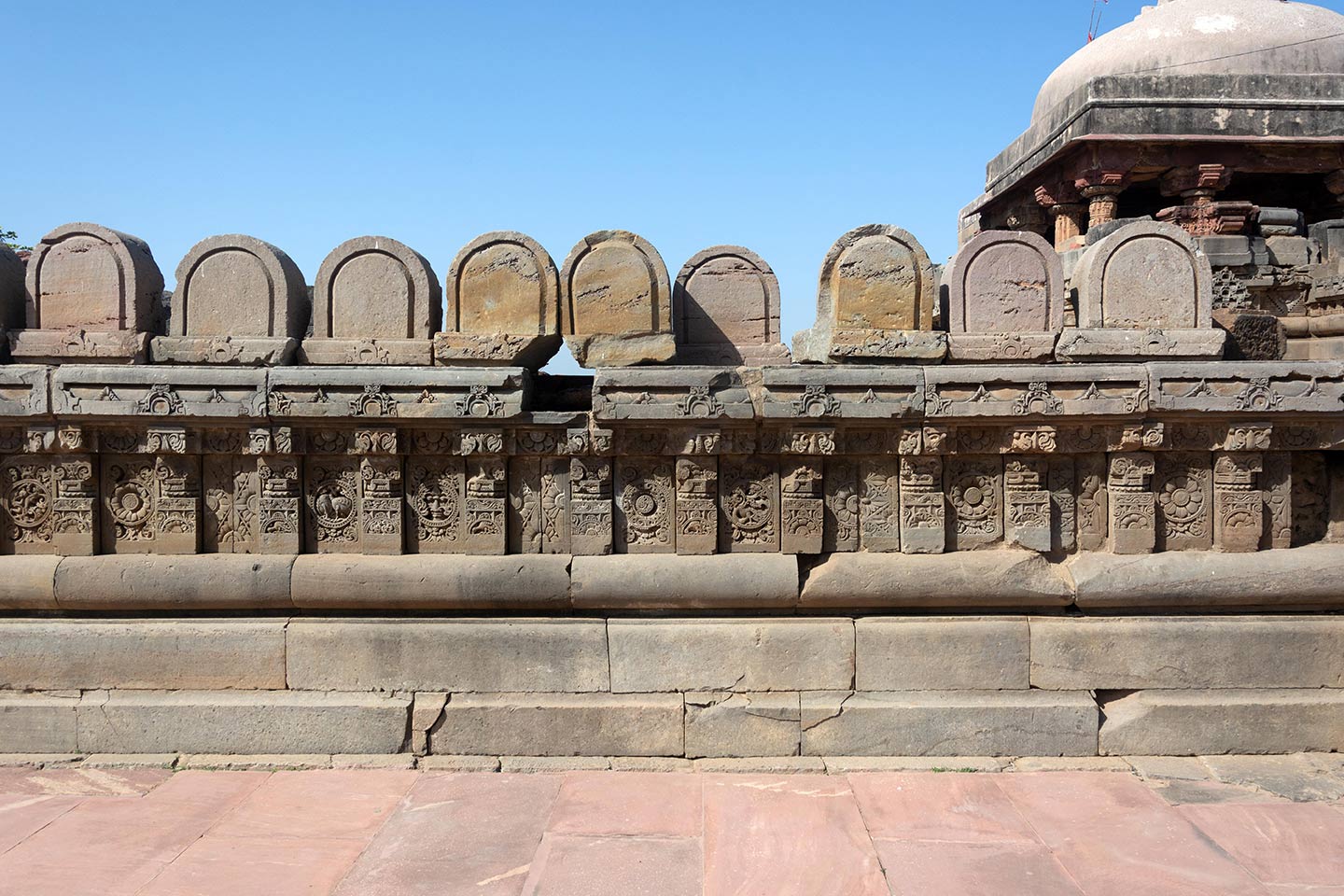 U-shaped rounded stones are assembled on the parapet, but their position or purpose in the original temple is unknown. The plaque's central artwork consists of a circular medallion surrounded by a foliage motif. Squat pillars, each featuring a square base, an octagonal shaft, and a square capital, divide the plaques.