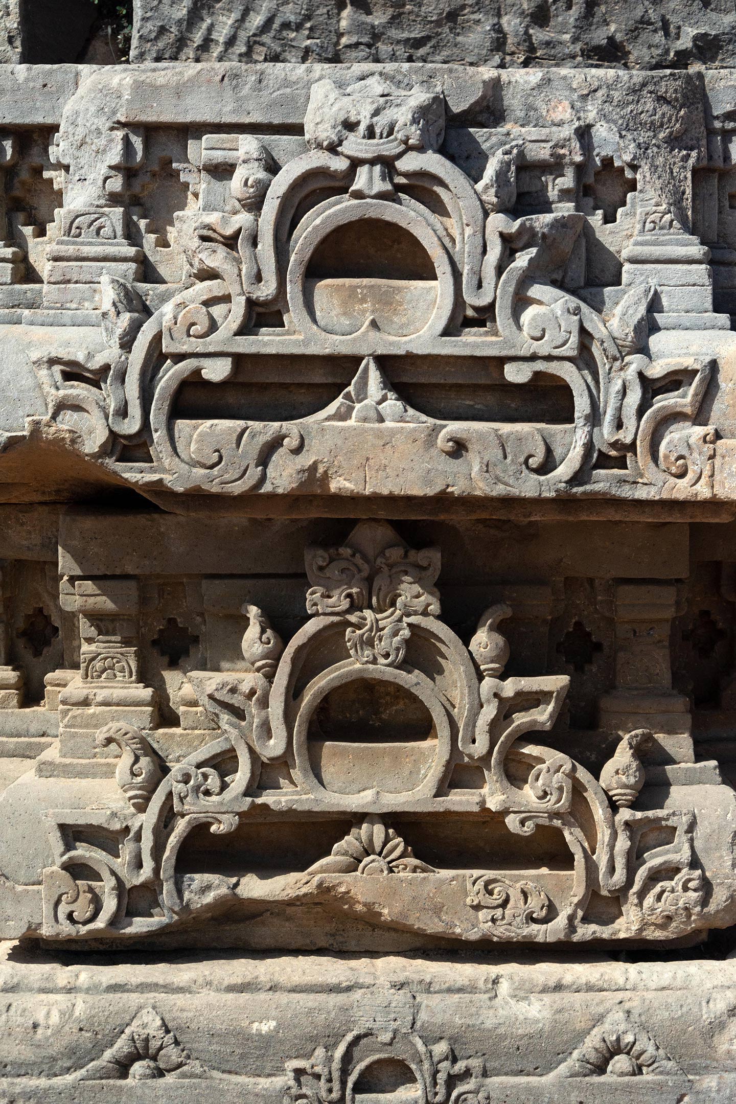 Broken debris from the original temple assembled on the northeast face of the adhisthana. The split gavaksha motifs in the carvings are visible.