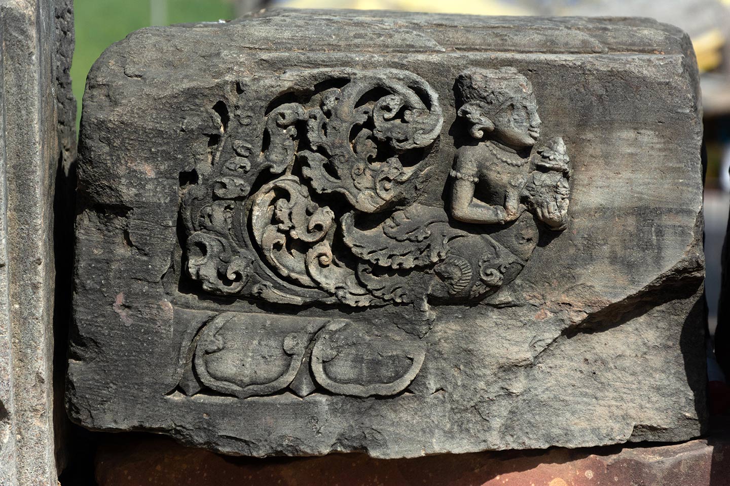 The carving features a kinnari holding a purna ghata (a symbol of abundance, prosperity, and fertility). The upper body of the kinnari is depicted with a female human figure, and the lower body consists of a bird, which forms a floral motif at the rear.