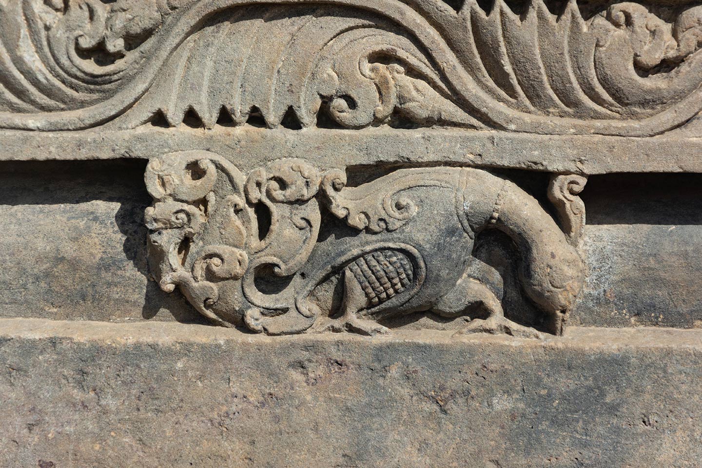 The bas relief depicts a peacock gathering food from the ground. The bird wears a ring around its neck.