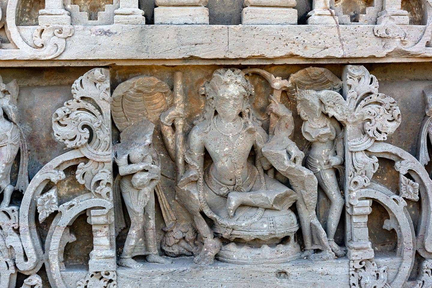 Image 1: The adhisthana has depictions of various Hindu gods and goddesses framed within elaborately carved panels. This panel has a central male figure holding a hala (plough) and large hooded nagas (serpents). The panel has a central male figure seated in the lalitasana posture on a circular throne. The figure has four arms and holds a hala (plough) in his upper left hand.