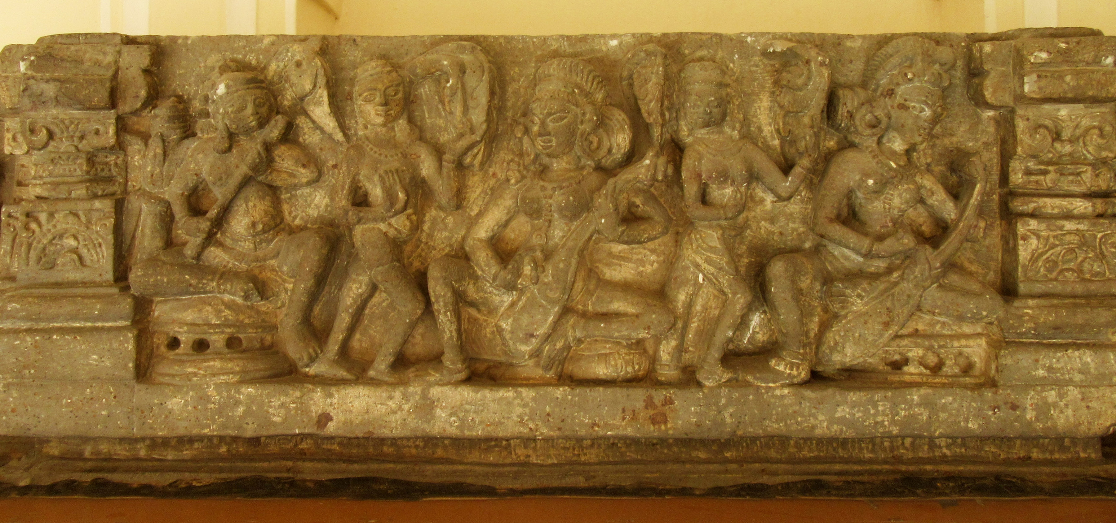 Image 5: Musicians, dancers, and harp players are present on the central section of the lintel. The right section has a depiction of Kubera with a female attendant serving wine; the left section has a seated Durga in a padmasana position on a lotus with eight hands holding a bow, kamandala (pitcher), sword, shield, and rosary.